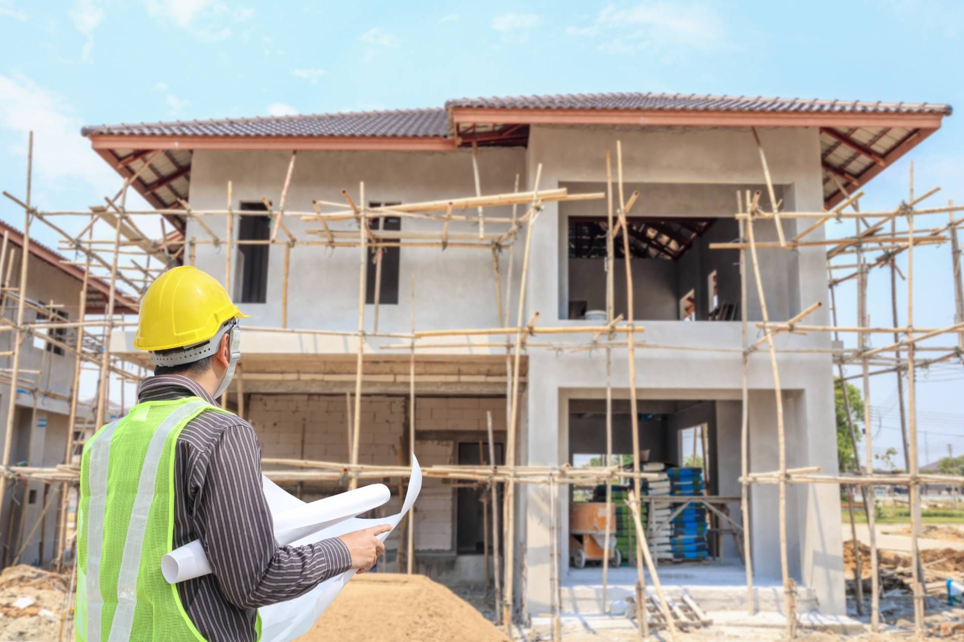 A construction worker is standing in front of a house under construction.