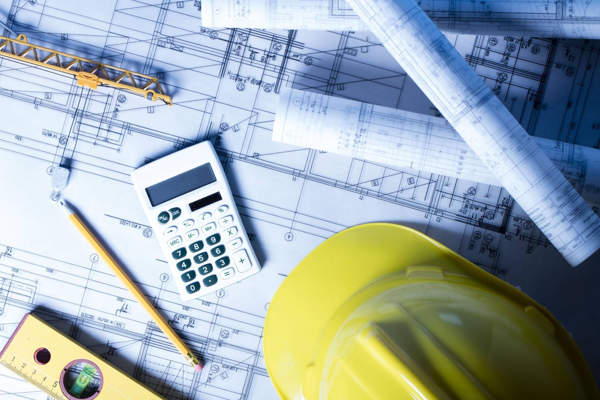 A hard hat a calculator a pencil and a level are on top of a blueprint.