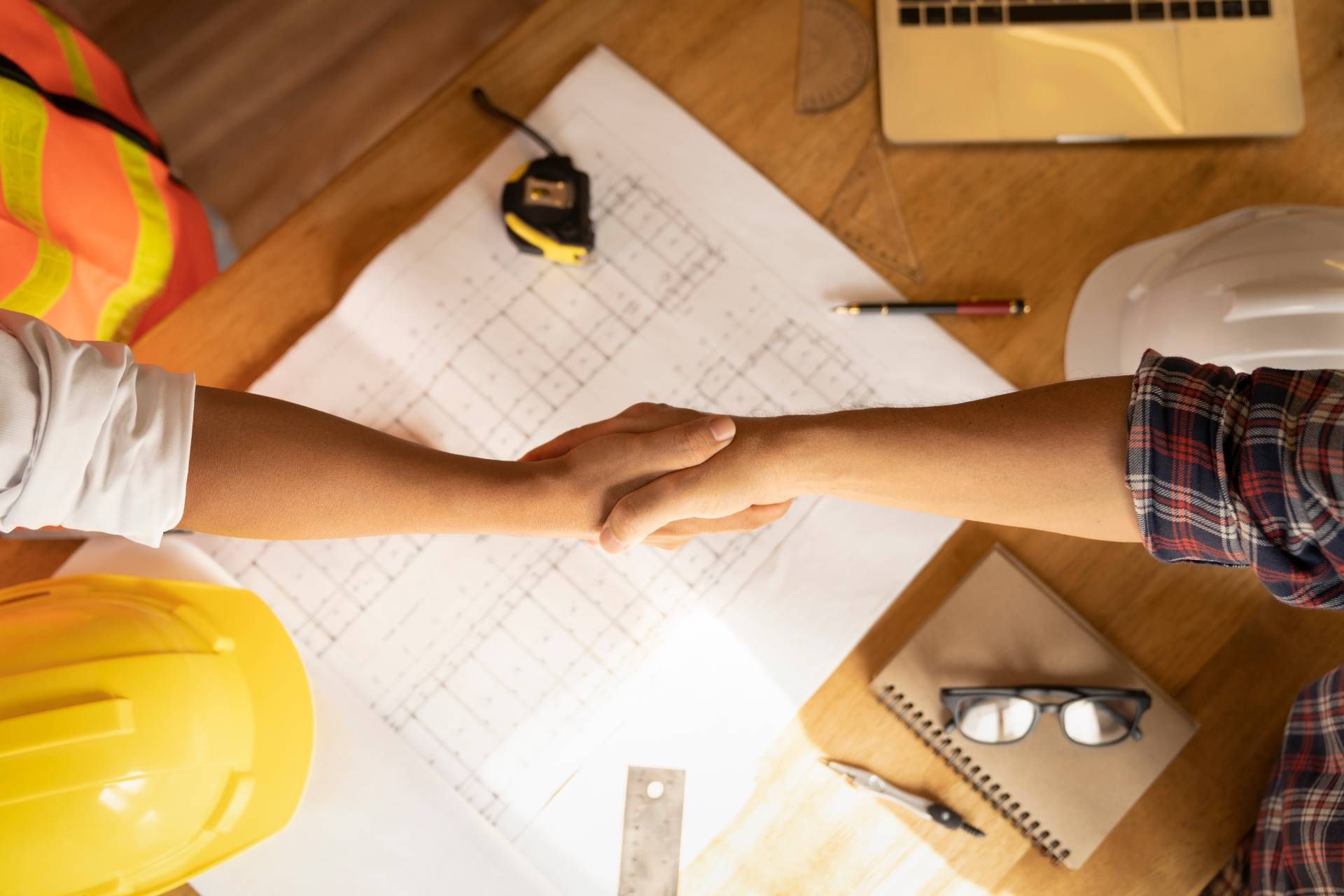 Two construction workers are shaking hands over a table.