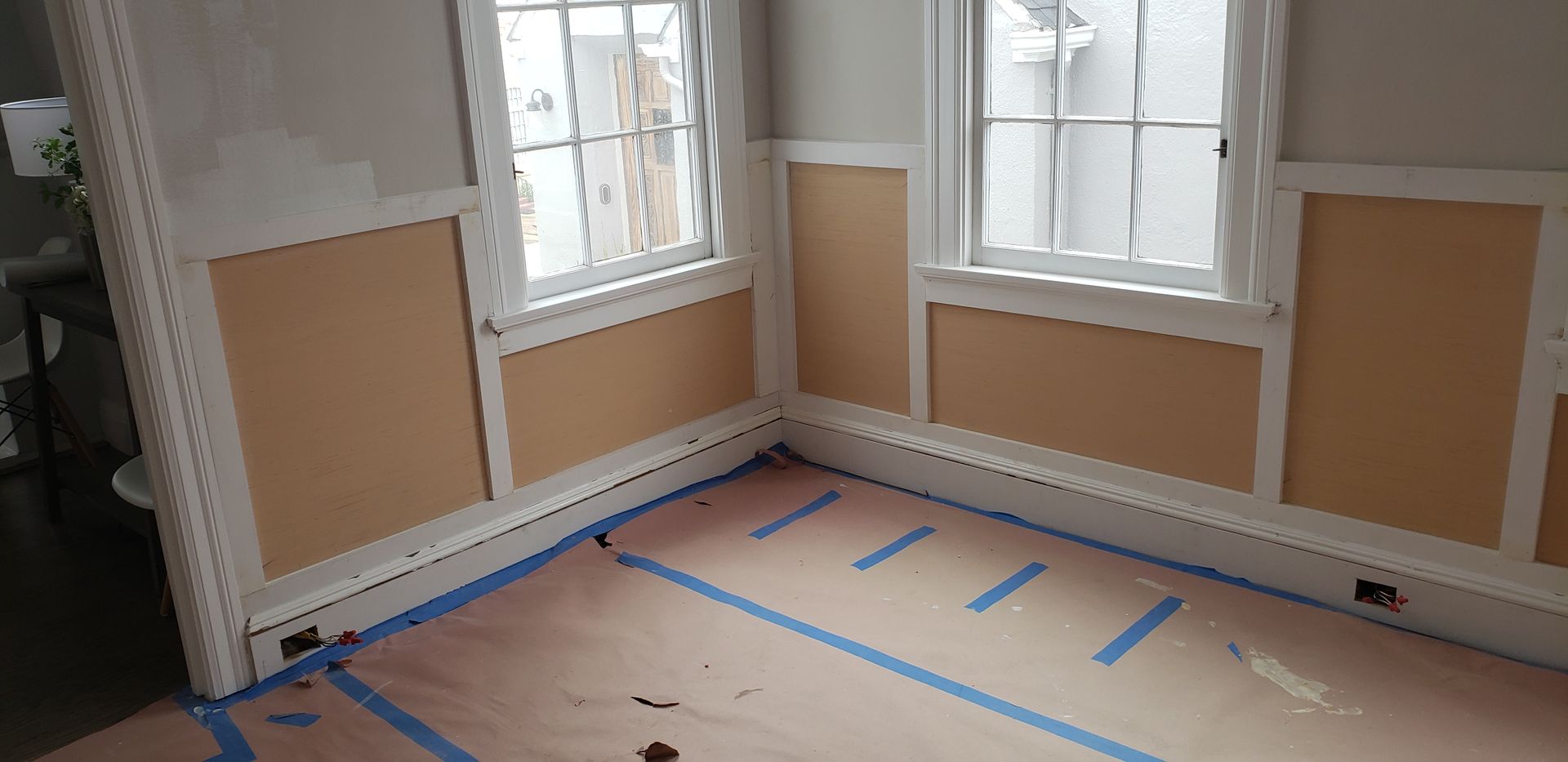 A carpenter measuring a wooden plank at a workshop, wearing a mask and apron.