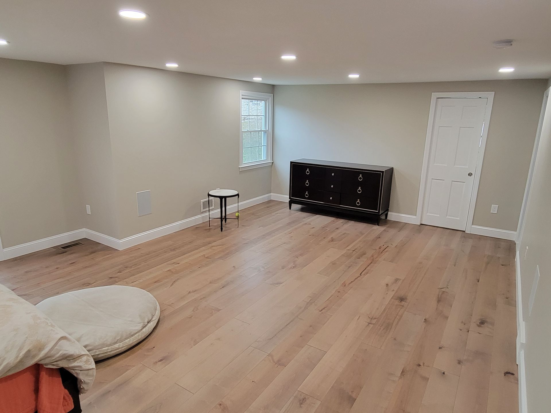 Empty room with wood floors, white walls, a black cabinet, and a small window.