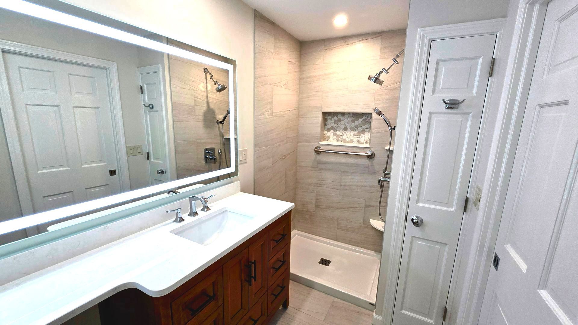 A bathroom with a sink , LED mirror and walk in shower.