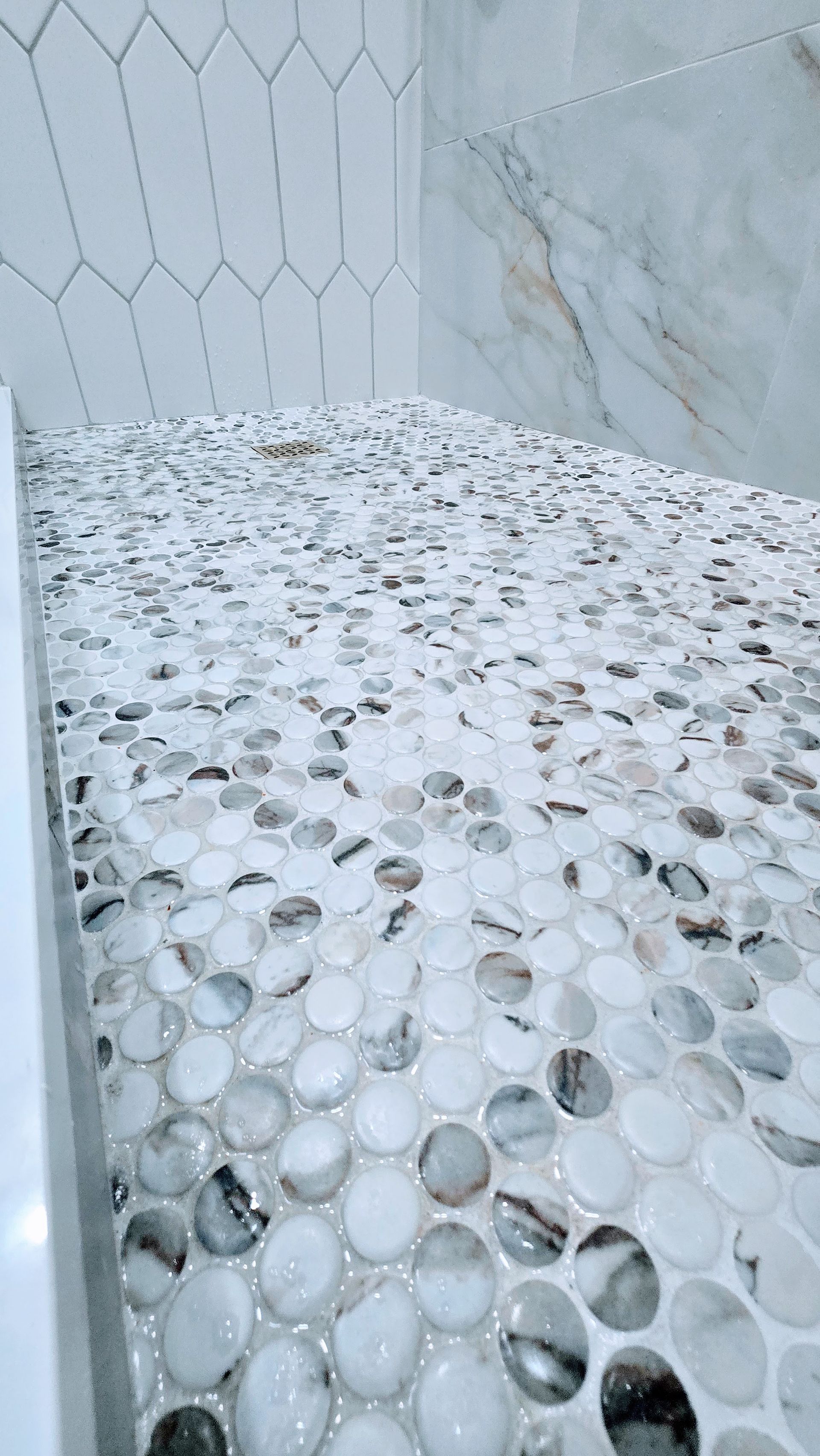 Shower with pebble mosaic floor and hexagon tile wall.