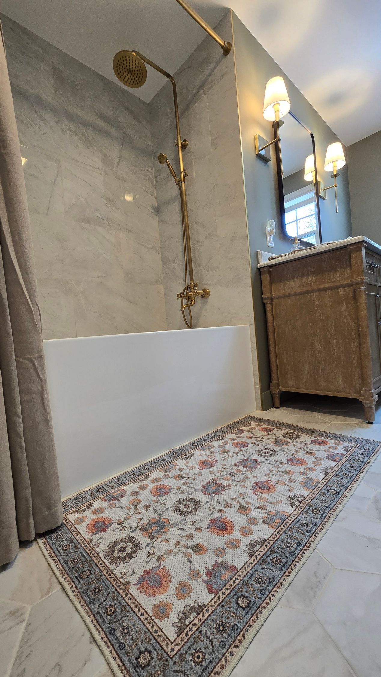 A bathroom with a bathtub , sink , mirror and rug.