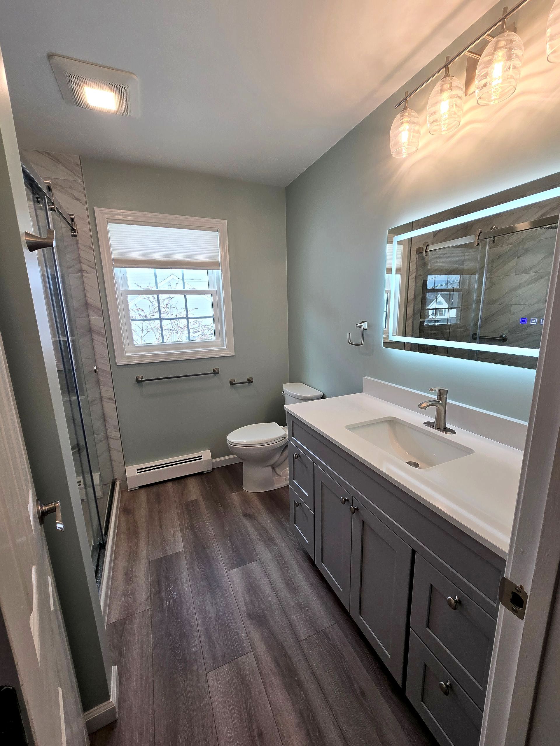 A bathroom with a sink , toilet , shower and led mirror.