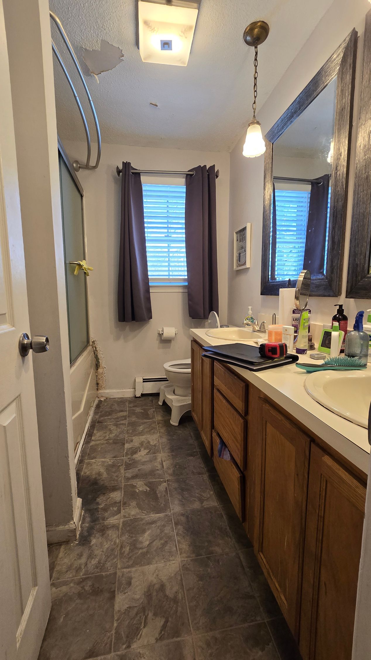 Bathroom with vanity, tub, and window. Gray tile floor, wood cabinets, and brown curtains.