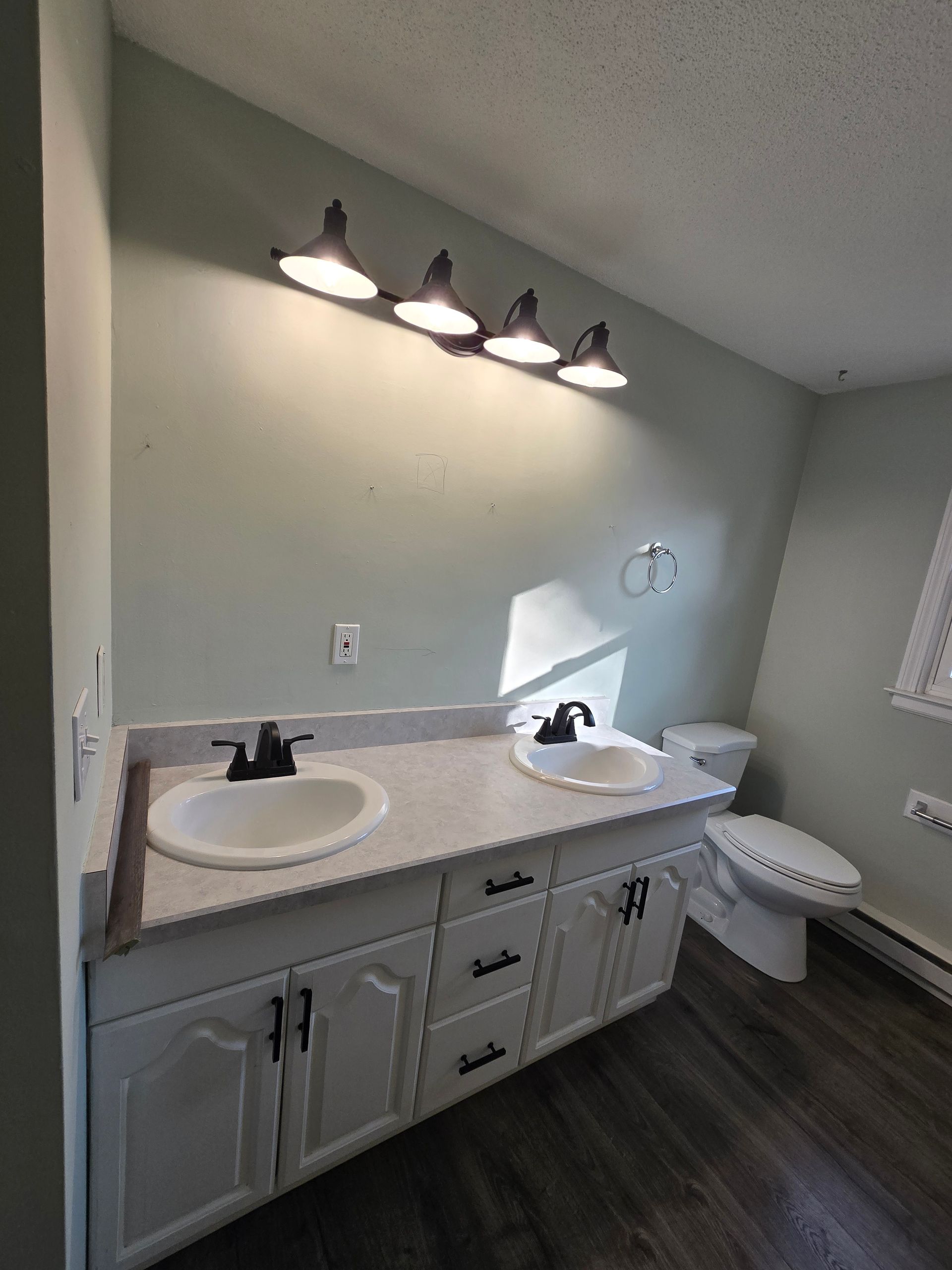A bathroom with two sinks , a toilet and a window.