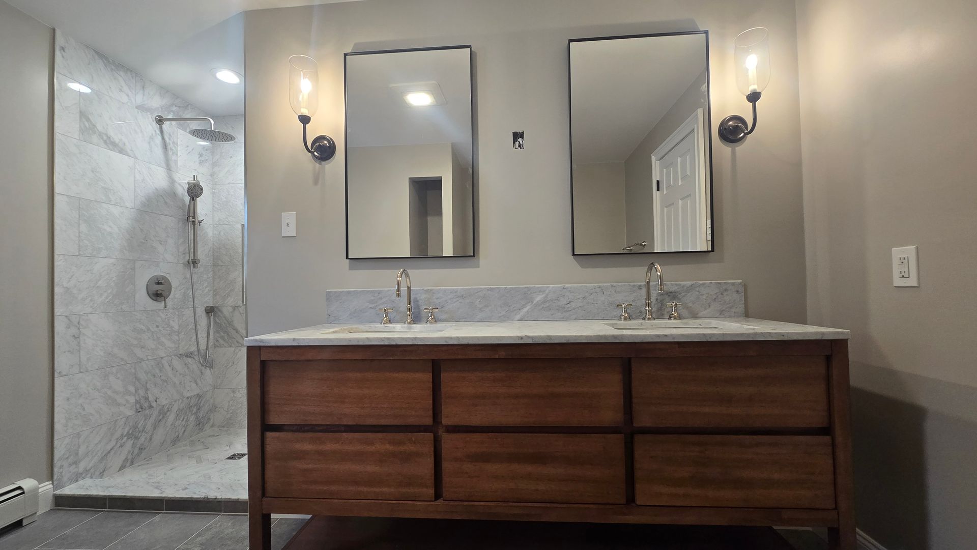 A bathroom with two sinks , two mirrors and a walk in shower.