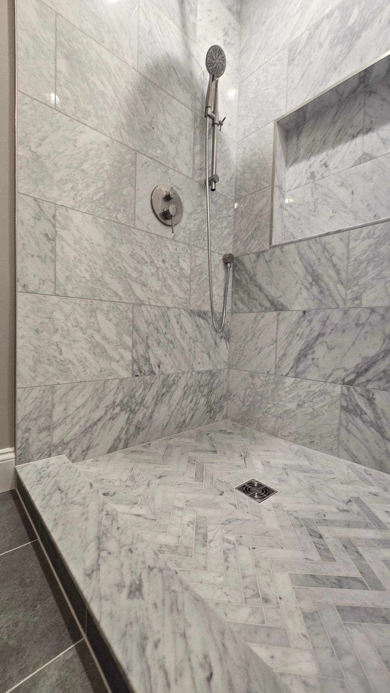 A bathroom with a walk in shower with marble tiles and a shower head.