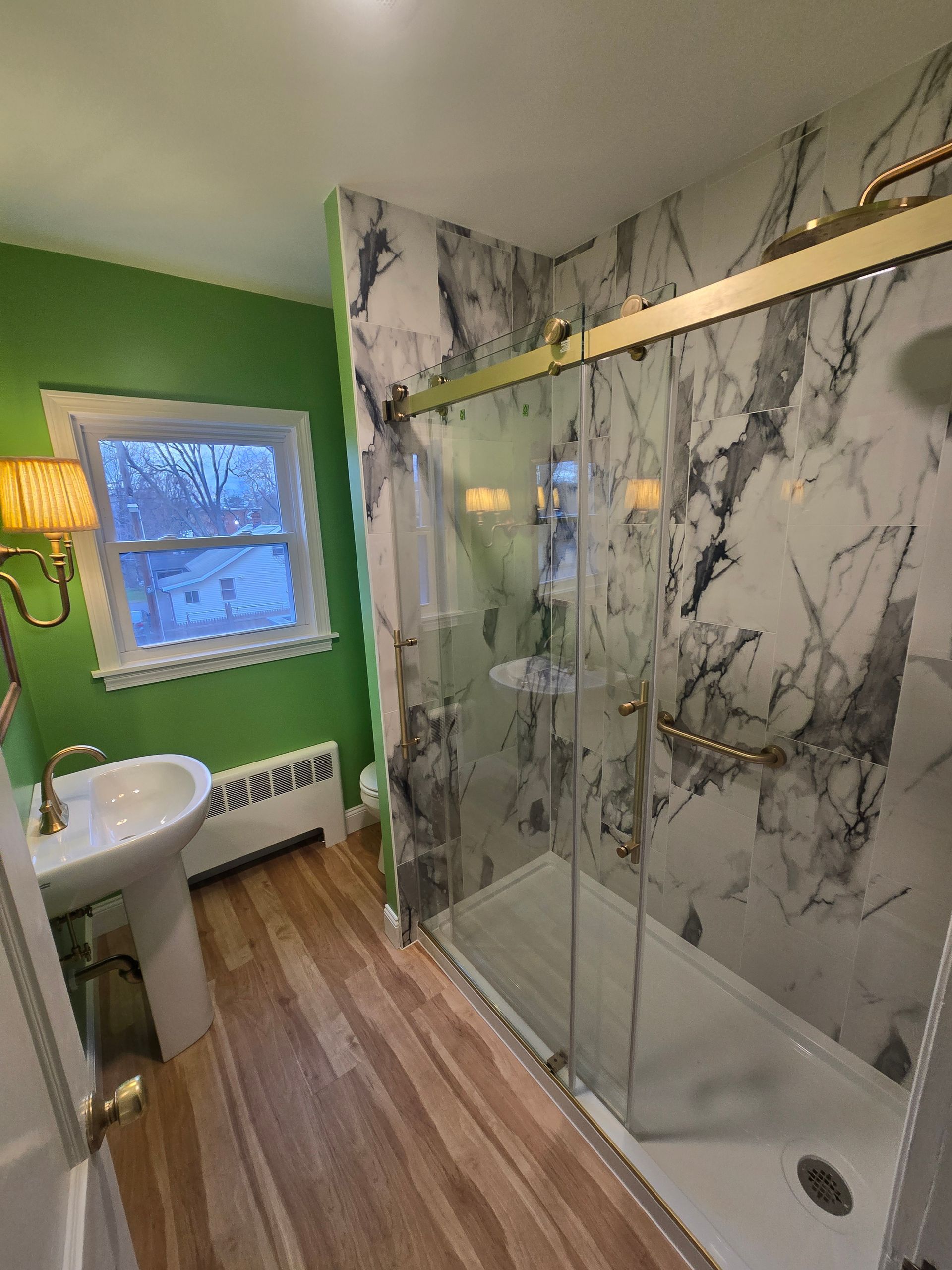 A bathroom with green walls , a sink , and a walk in shower.