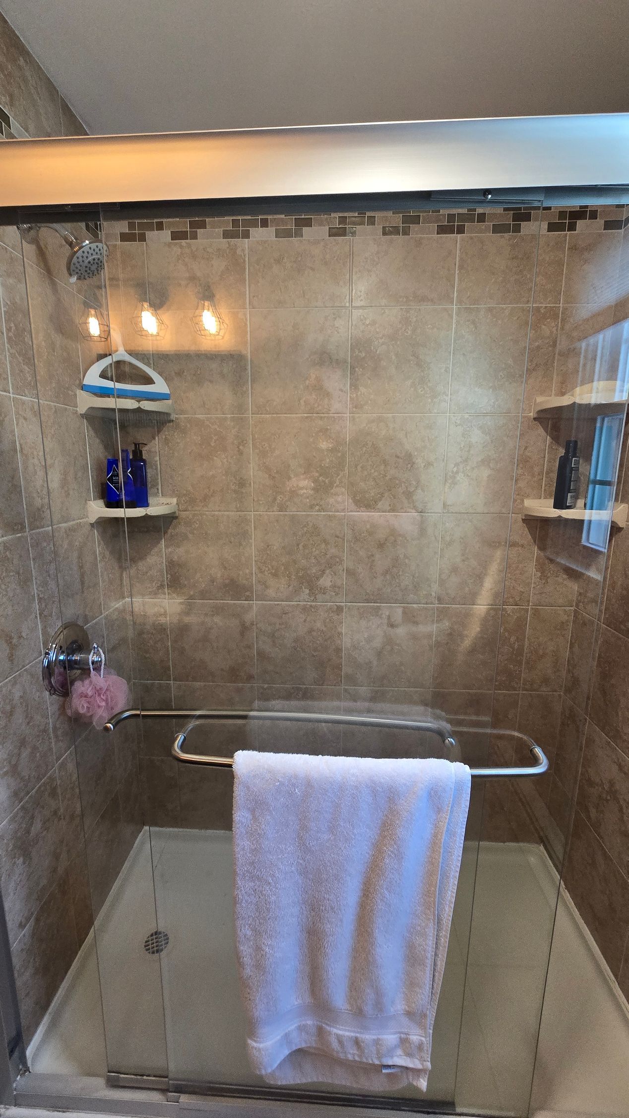 Shower interior with a towel hanging, shelves with toiletries, and beige tiles.
