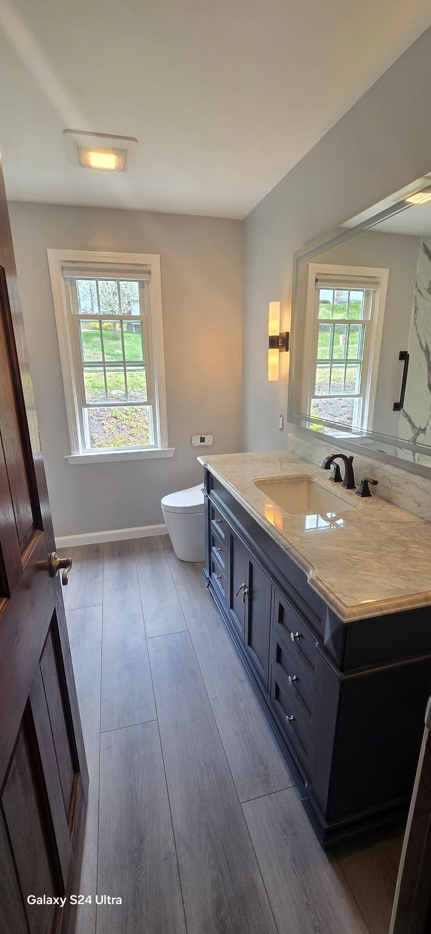 A bathroom with a sink , toilet , mirror and window.