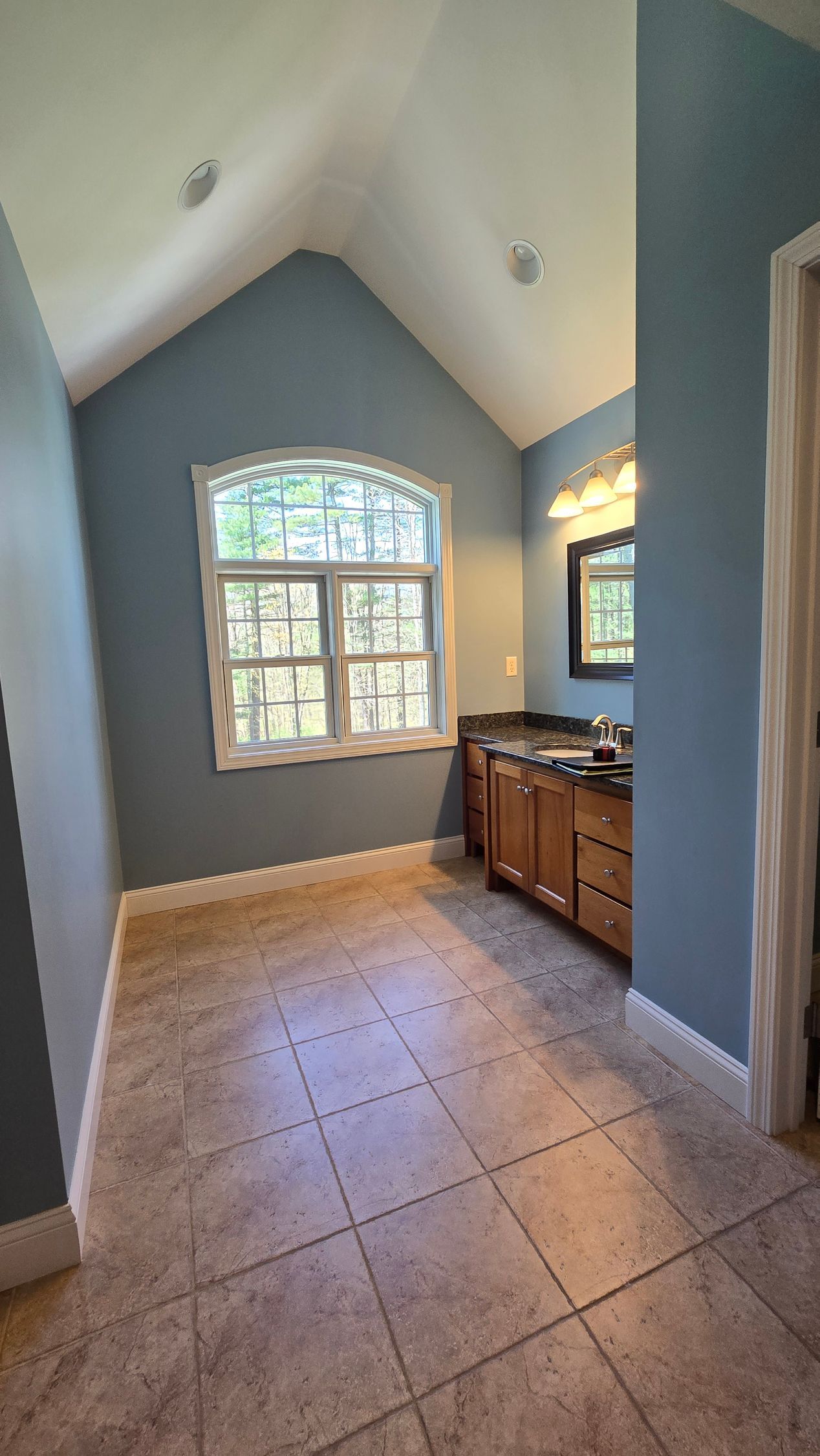 Bathroom in Glastonbury, CT with blue walls, window, vanity, and tan tile floor.