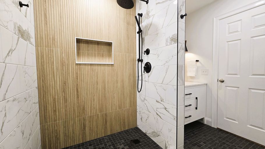 Modern bathroom in Berlin, CT with marble and wood-look tiles, black fixtures, and a glass shower door.
