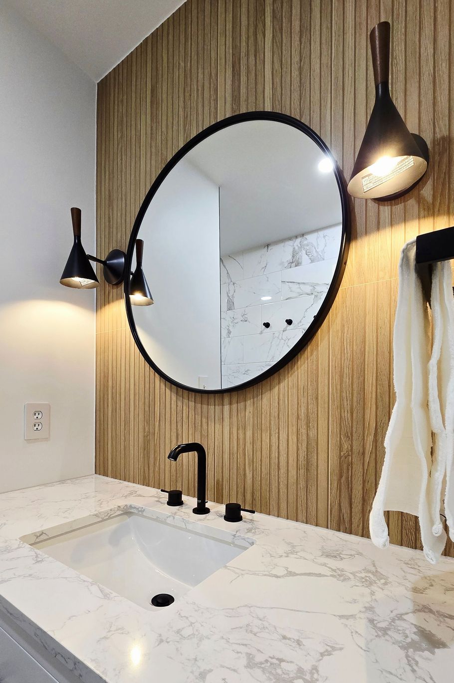 Bathroom in Berlin, CT with oval mirror, black fixtures, and wood-grain accent wall.