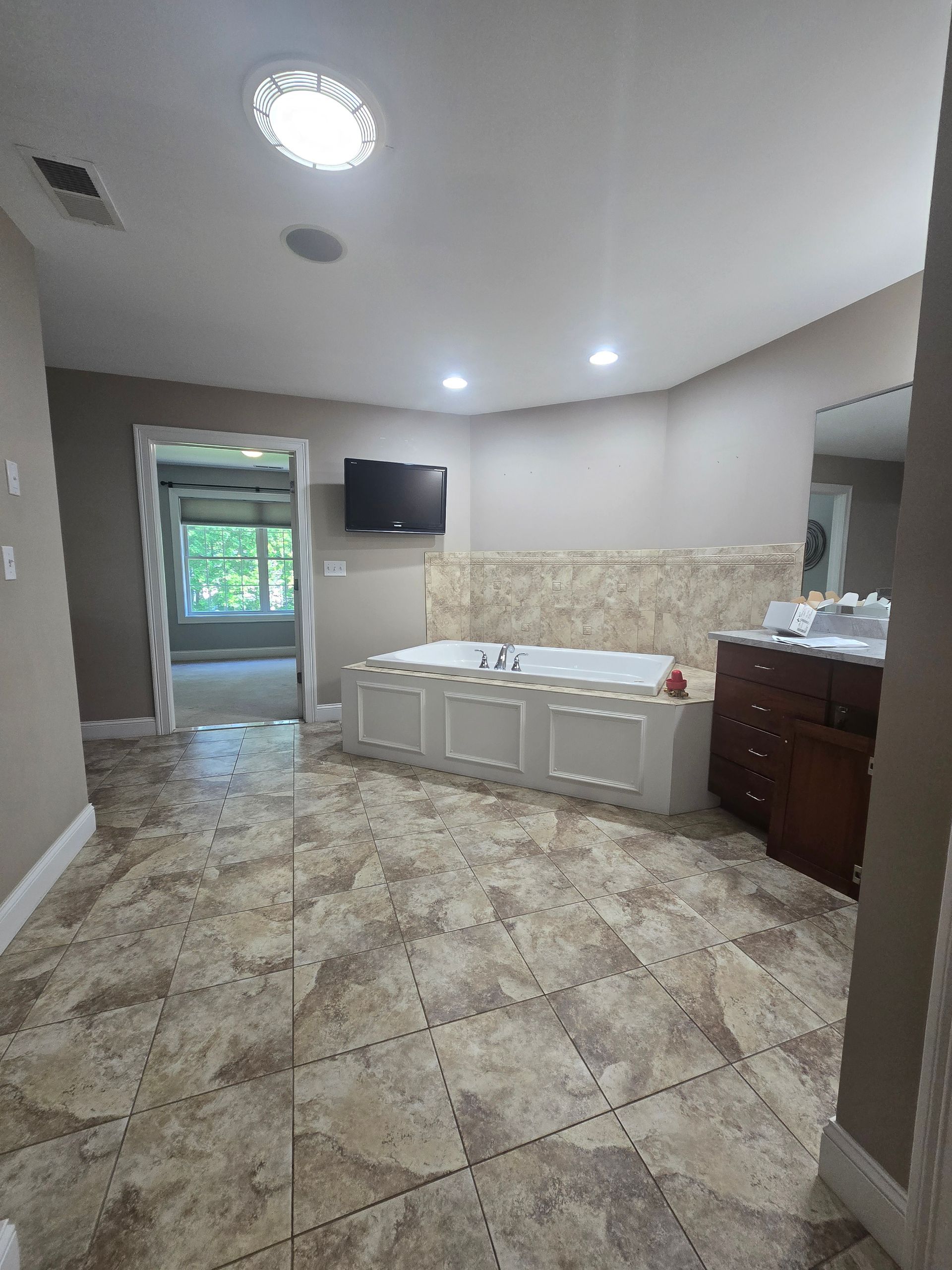 A bathroom with a jacuzzi tub , sink , mirror and television.