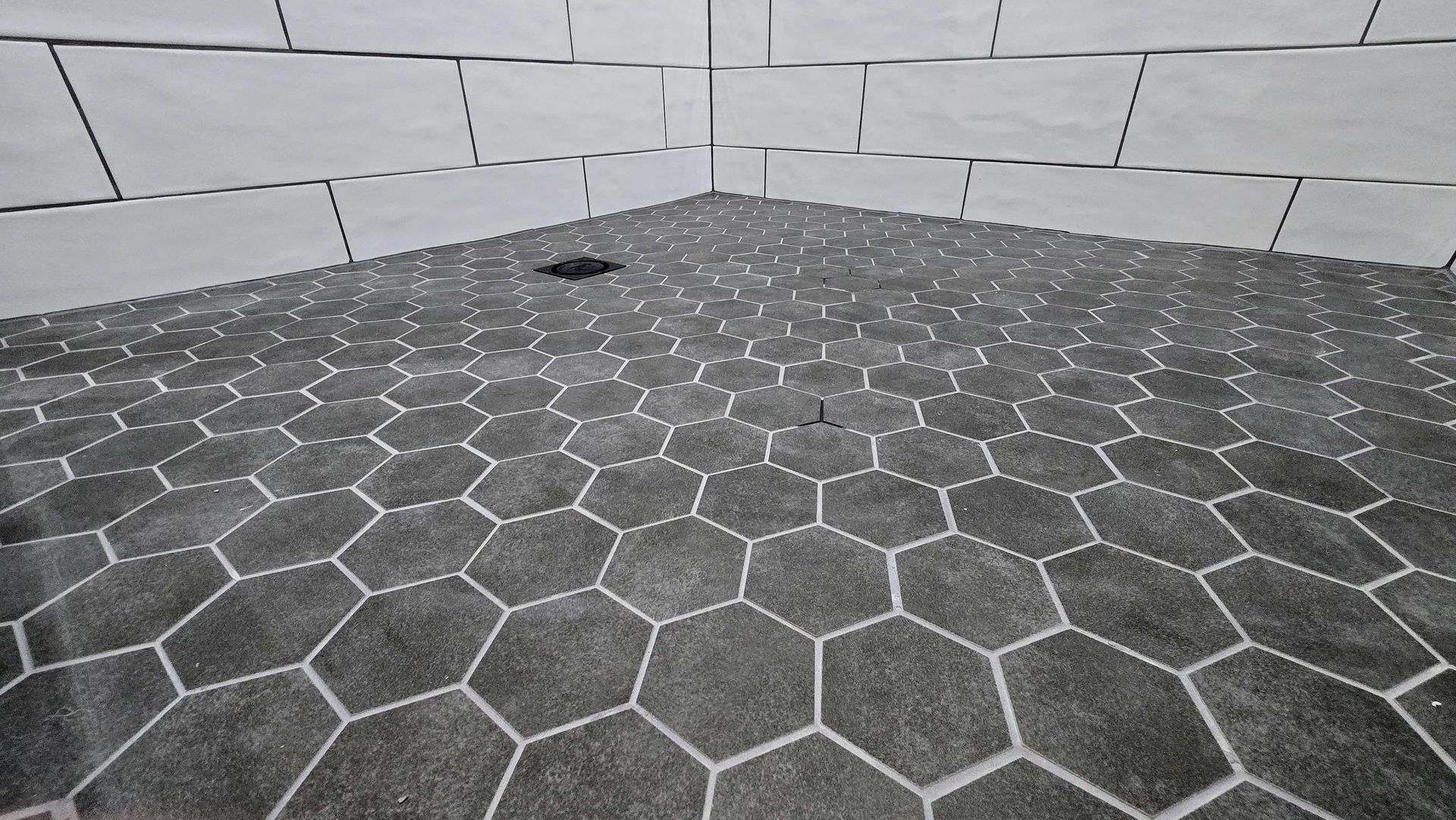 A black mosaic tiles on the shower floor and white photo of a tiled floor with a honeycomb pattern.