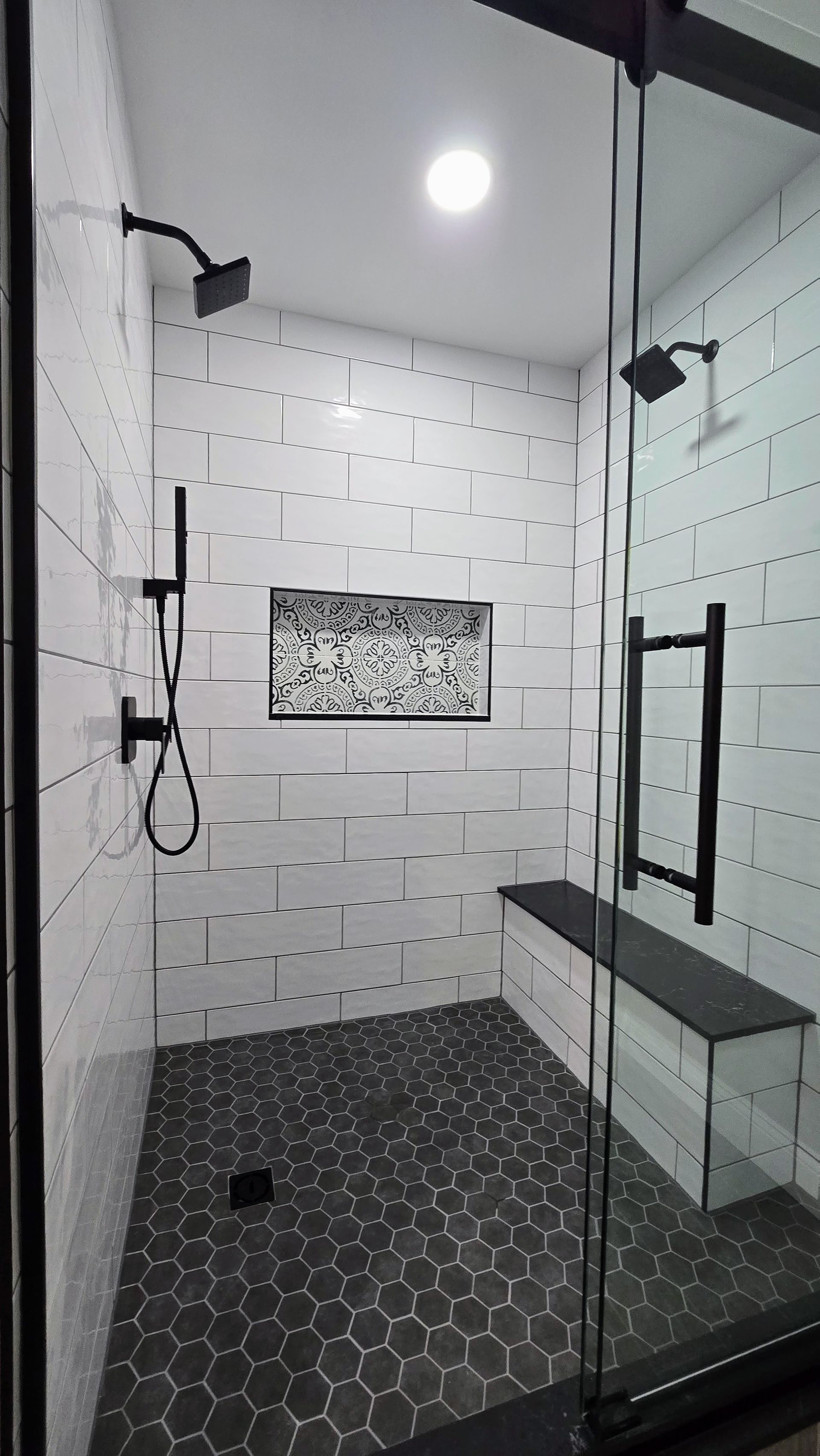 A black and white shower with a glass door and a bench.