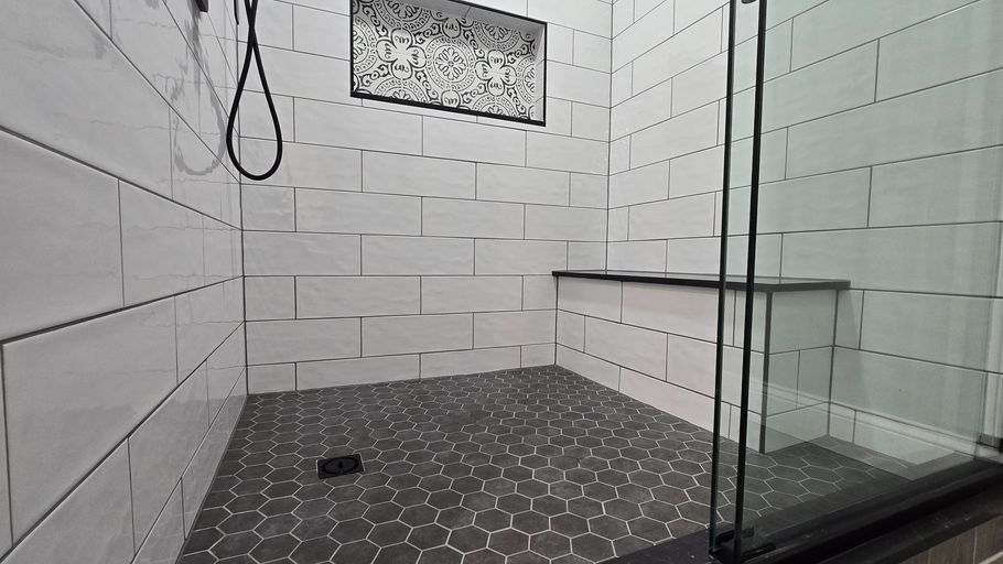 Modern walk-in shower in Southington, CT with white tiled walls, dark gray floor, glass door, and built-in bench.