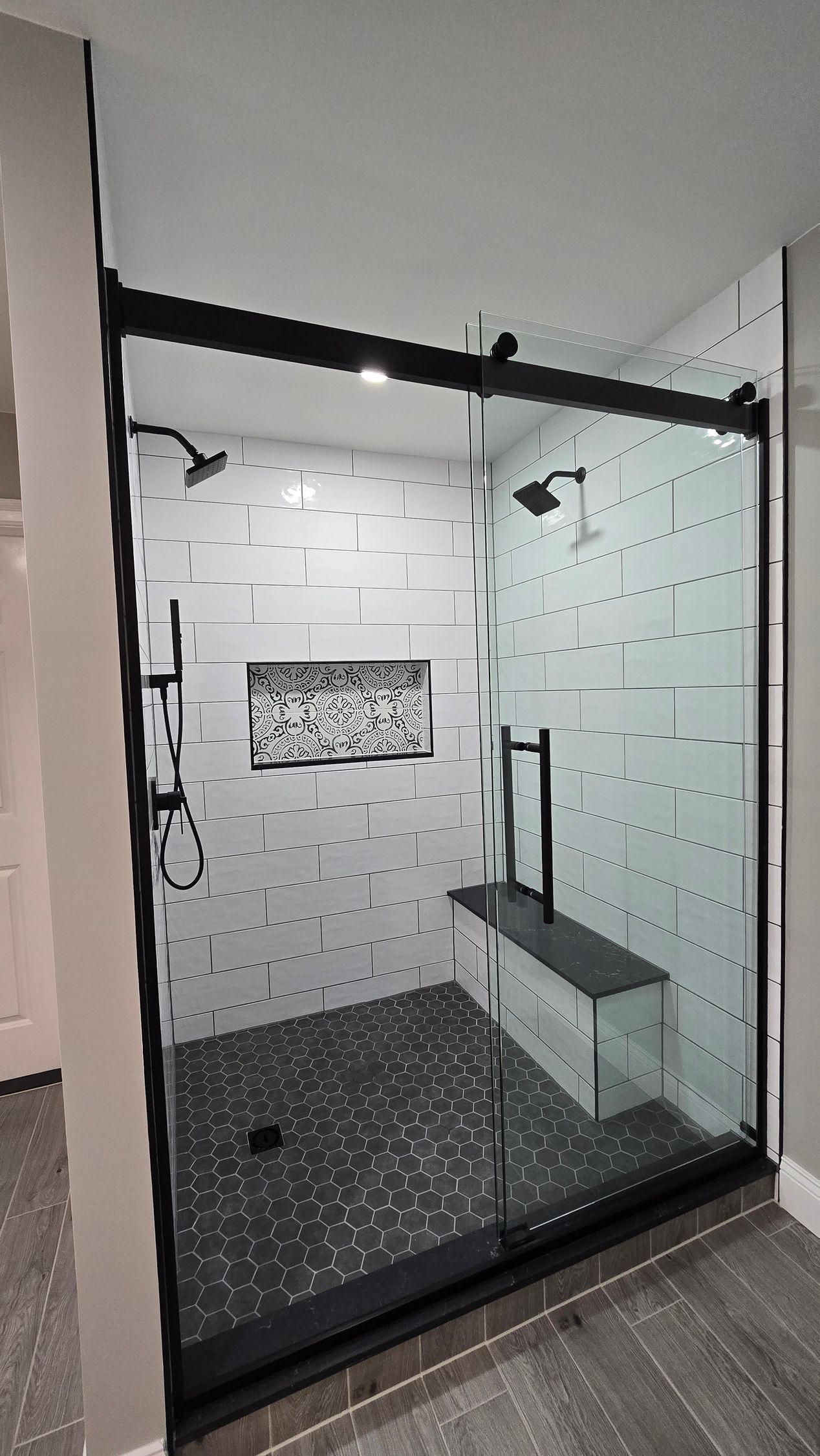 A walk in shower with a black frame and sliding glass doors.
