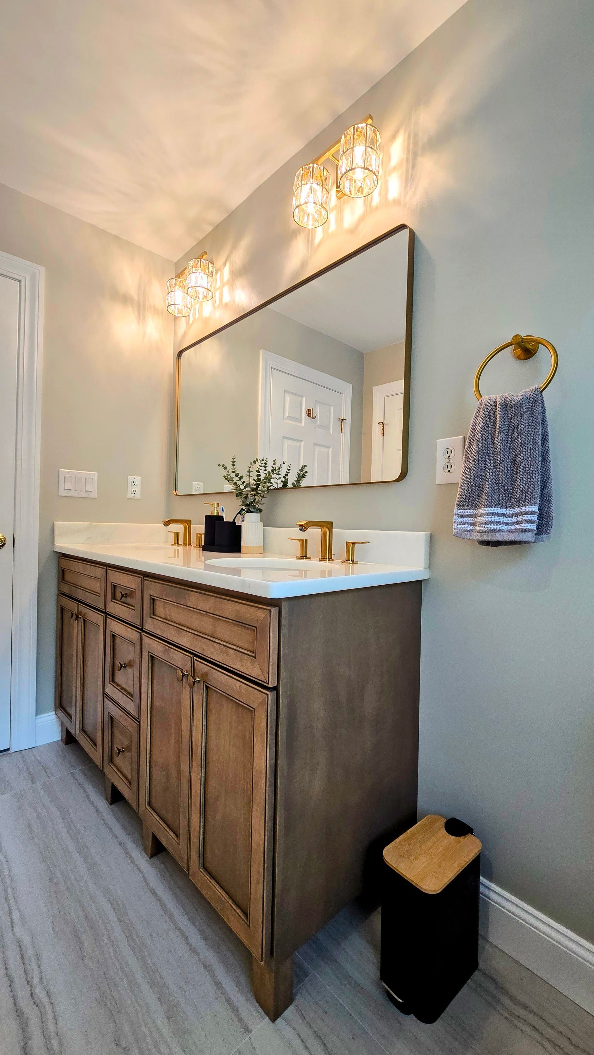 A rustic wood bathroom vanity in Cheshire, CT with a white marble countertop, gold faucet, and a large mirror under gold wall lights.