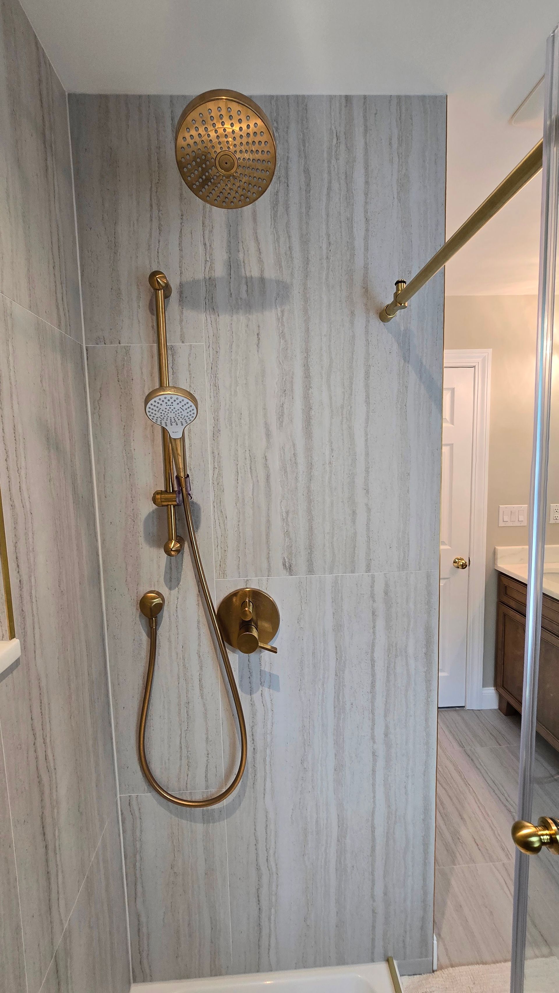 A modern shower with gold fixtures in Cheshire, CT, a rainfall showerhead, a handheld sprayer, and vertical gray-toned tile walls.