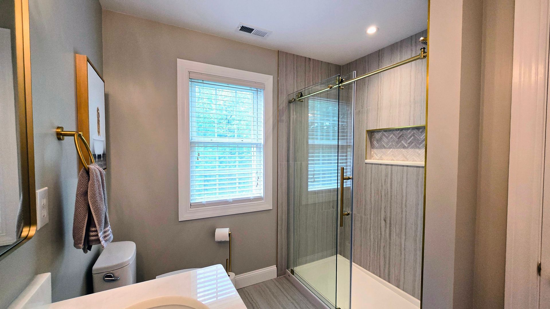 A modern bathroom in Cheshire, CT with a glass-enclosed shower featuring vertical tile, a white toilet, and a window with blinds.