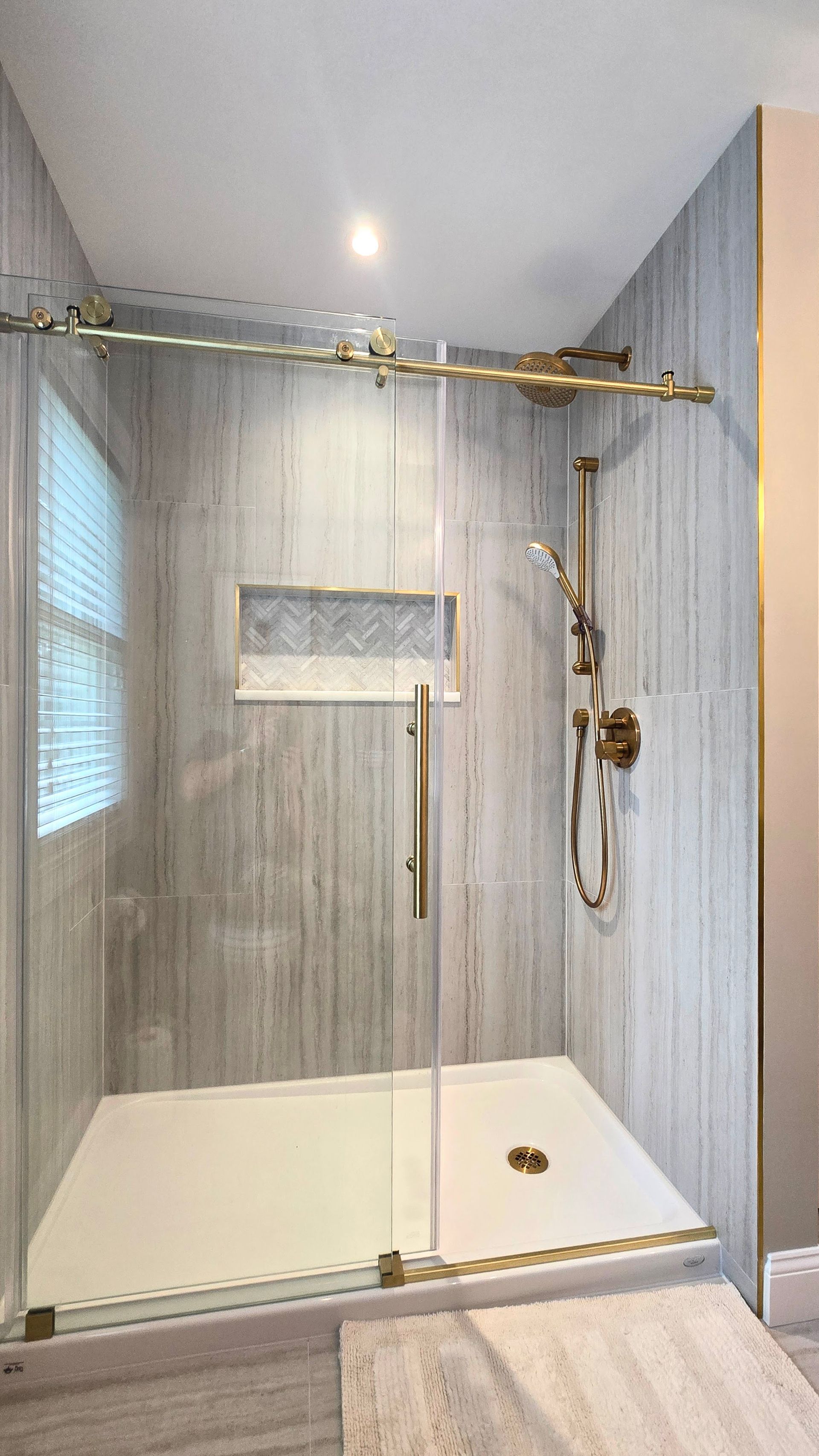 A modern walk-in shower in Cheshire, CT with grey vertical tile walls, a gold sliding glass door, and gold shower fixtures.
