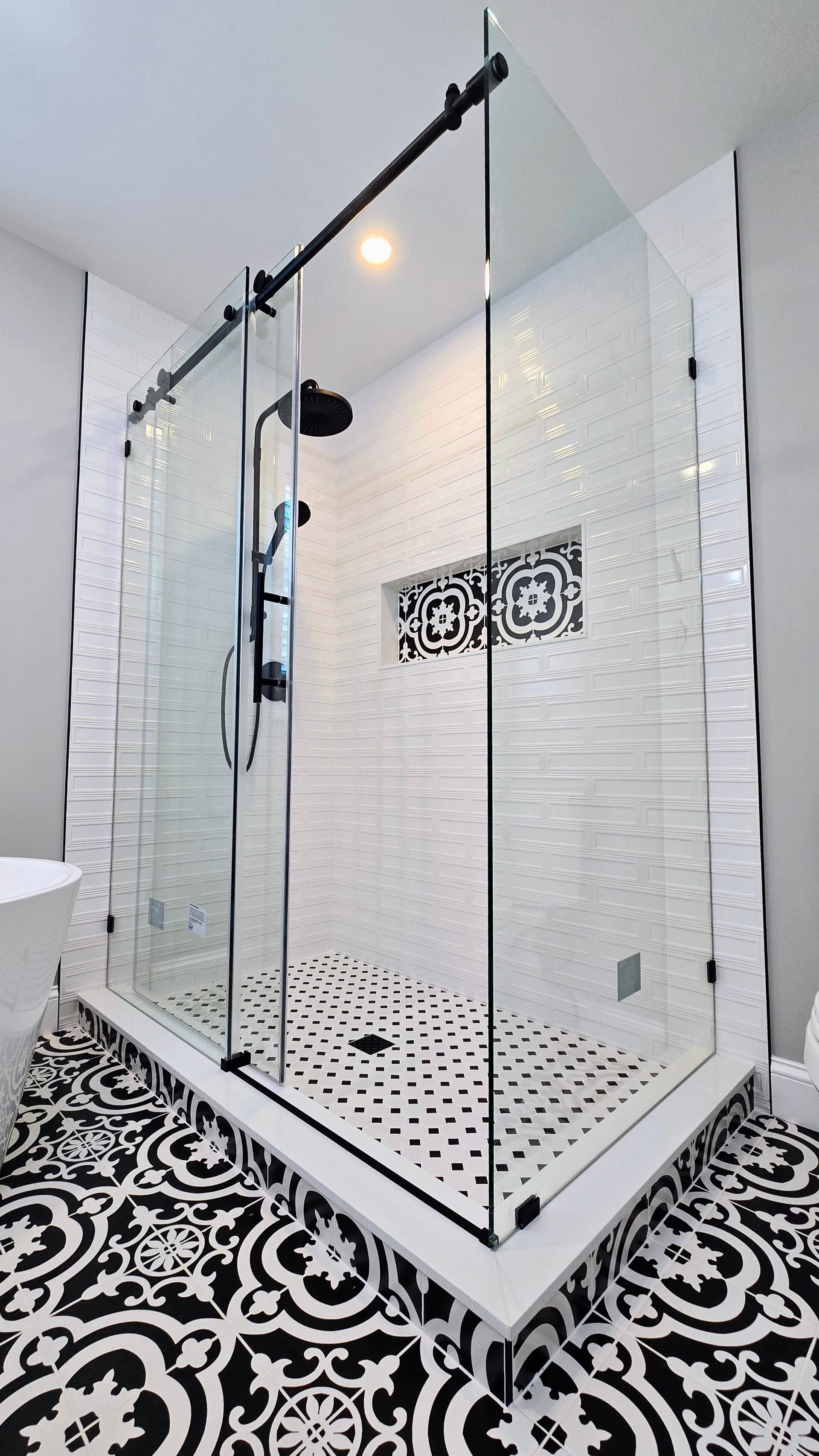 A bathroom with a walk in shower with sliding glass doors and a black and white tile floor.