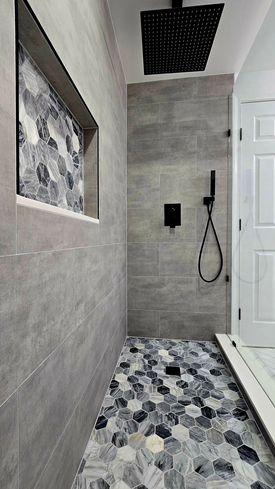 Gray tiled walk-in shower in West Hartford, CTwith mosaic floor and black fixtures, featuring a recessed shelf.