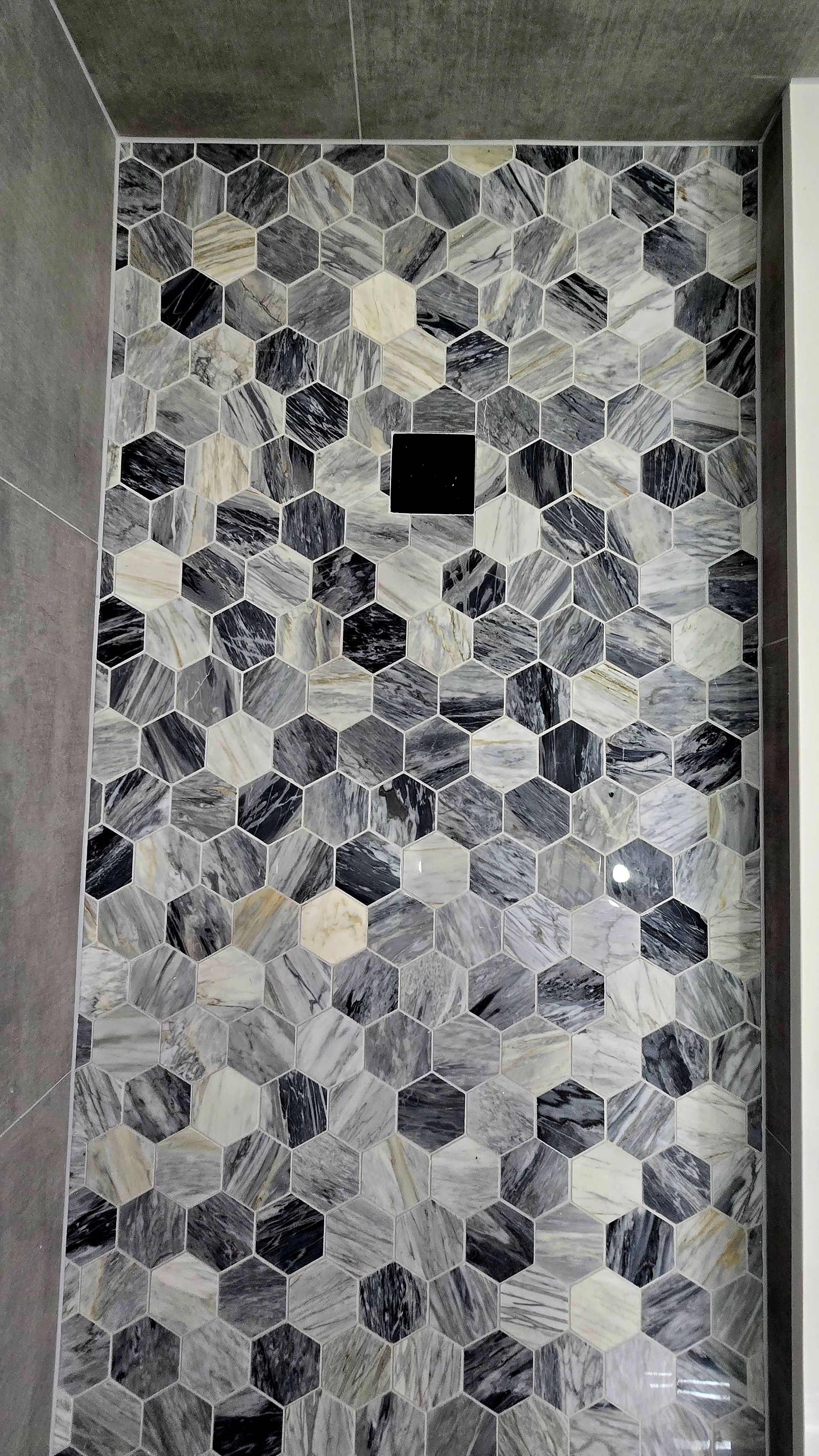 Shower floor remodel in West Hartford, CT featuring gray and white hexagon marble tiles surrounding a square black drain centered in the middle.