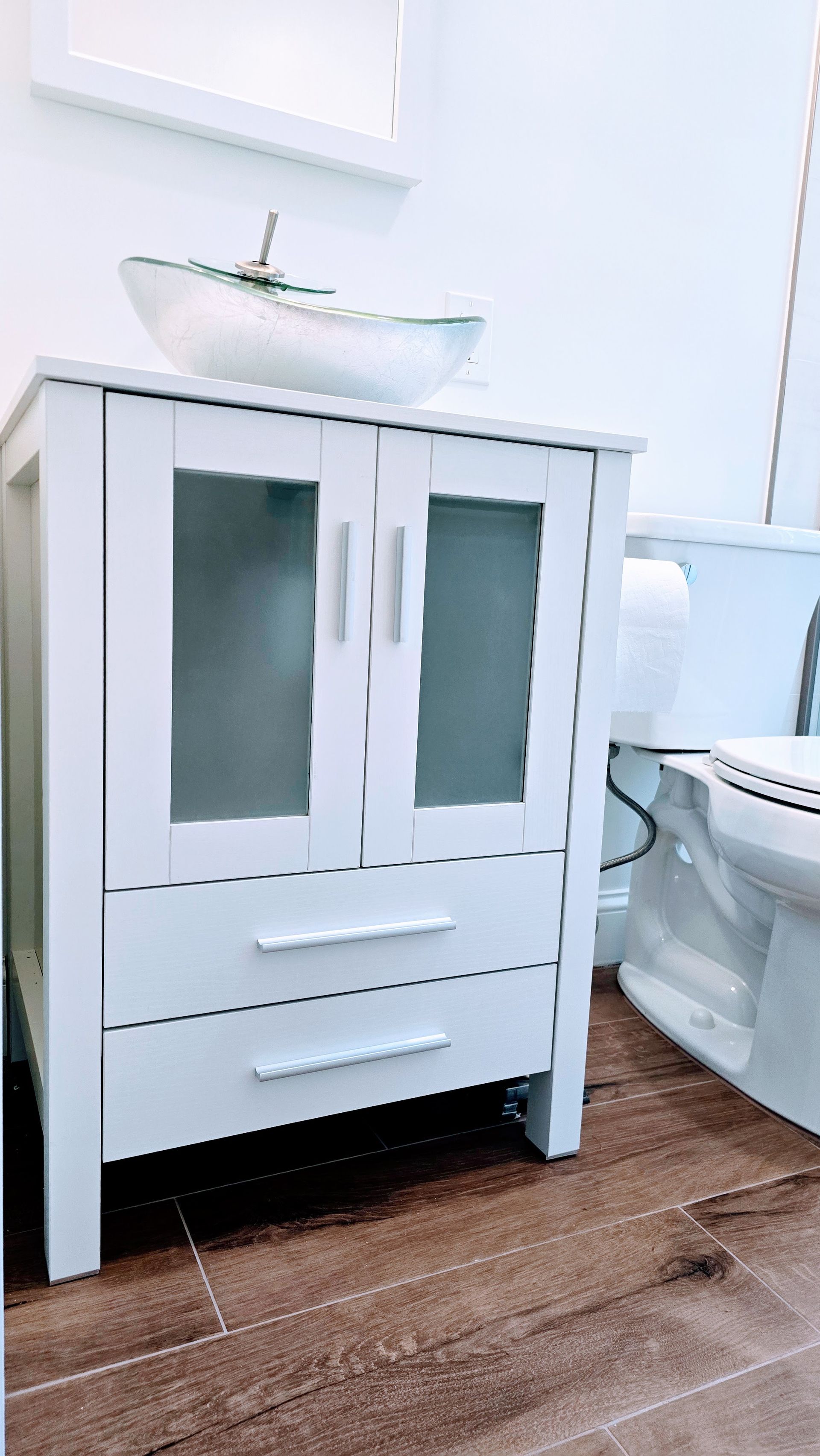 White bathroom vanity with frosted glass door panels and drawers, topped with a boat-shaped sink. Next to a white toilet.