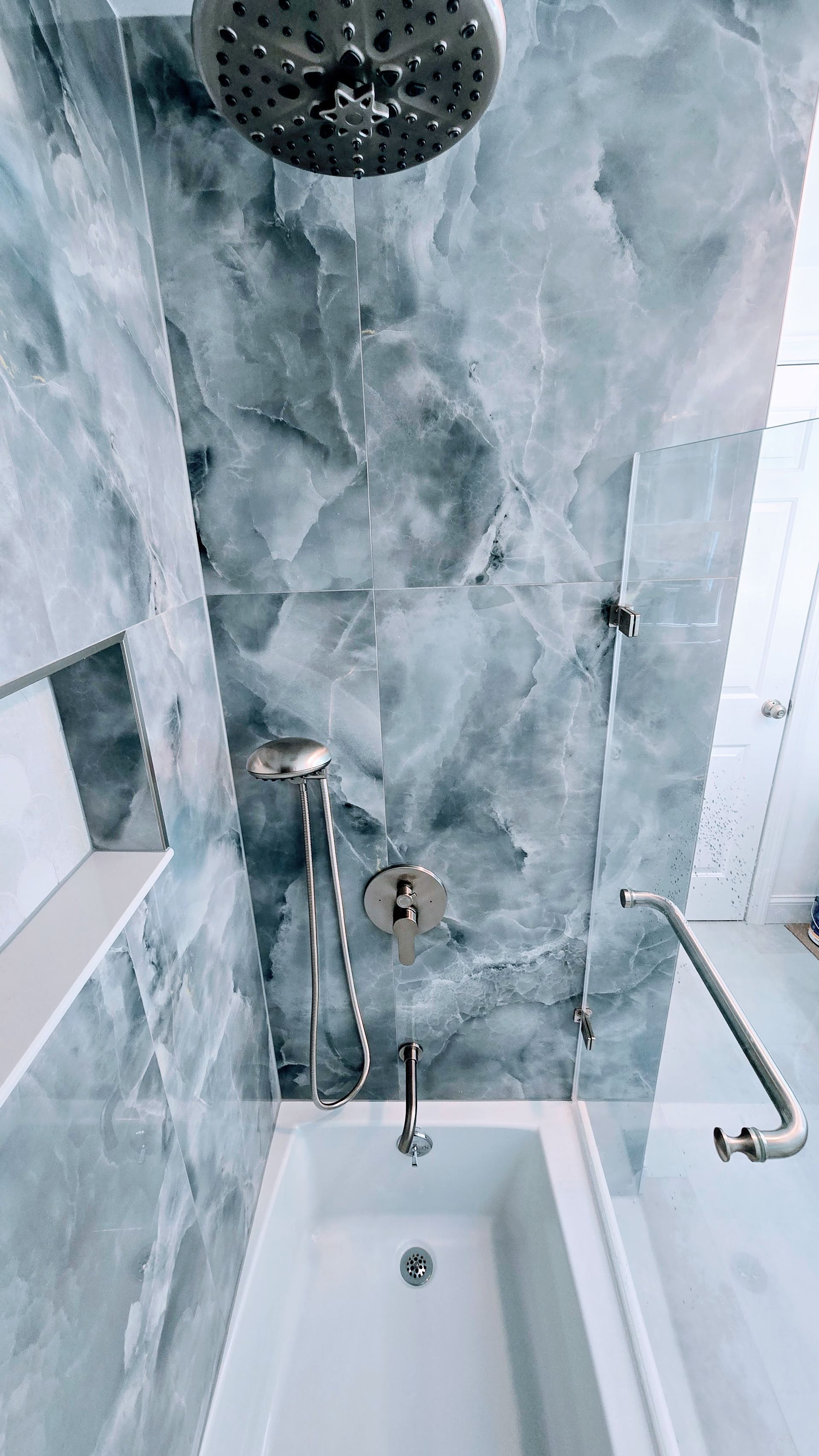 Bathroom with a white bathtub, silver shower fixtures, and walls covered in blue marble tiles.