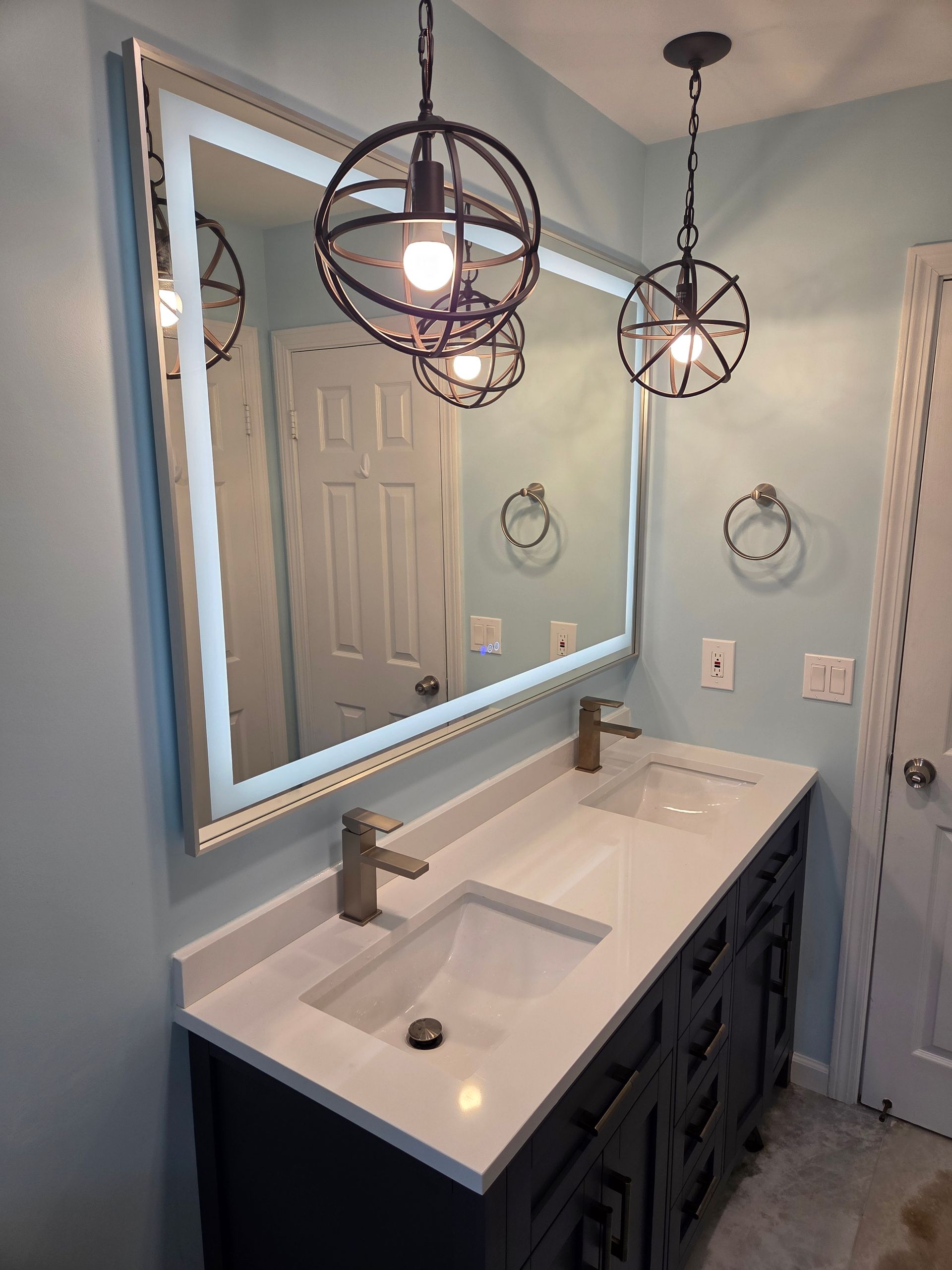 Bathroom with blue walls, a vanity with two sinks, and two globe pendant lights.