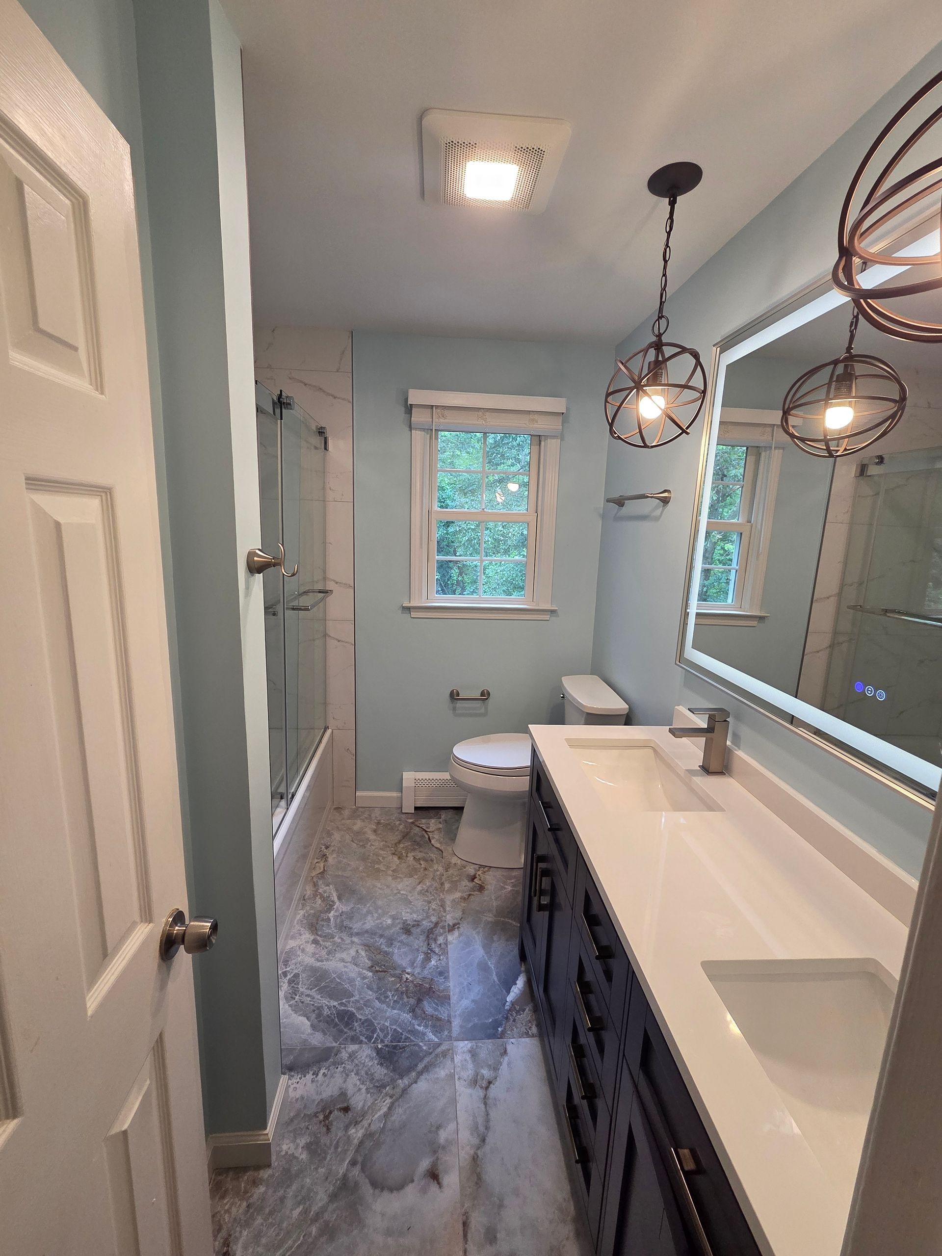 Bathroom with blue walls, dark vanity, and marble-patterned floor.  A window and a large mirror are present.