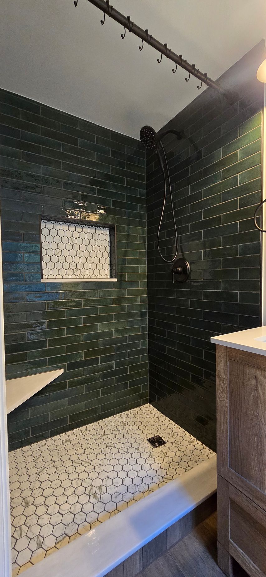 Shower with green brick tiles, mosaic floor, and dark fixtures.