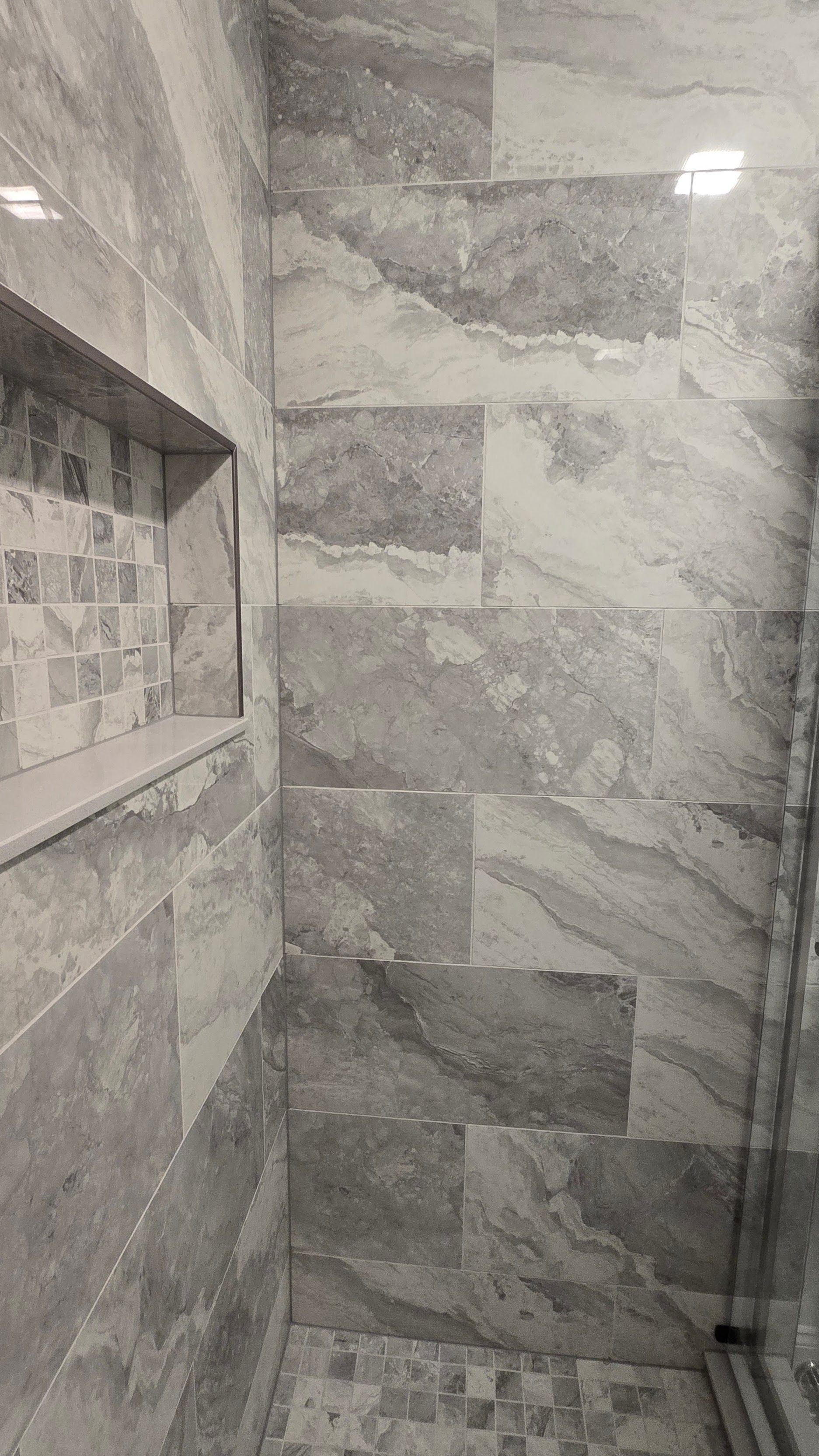 Gray tiled shower with a built-in shelf.