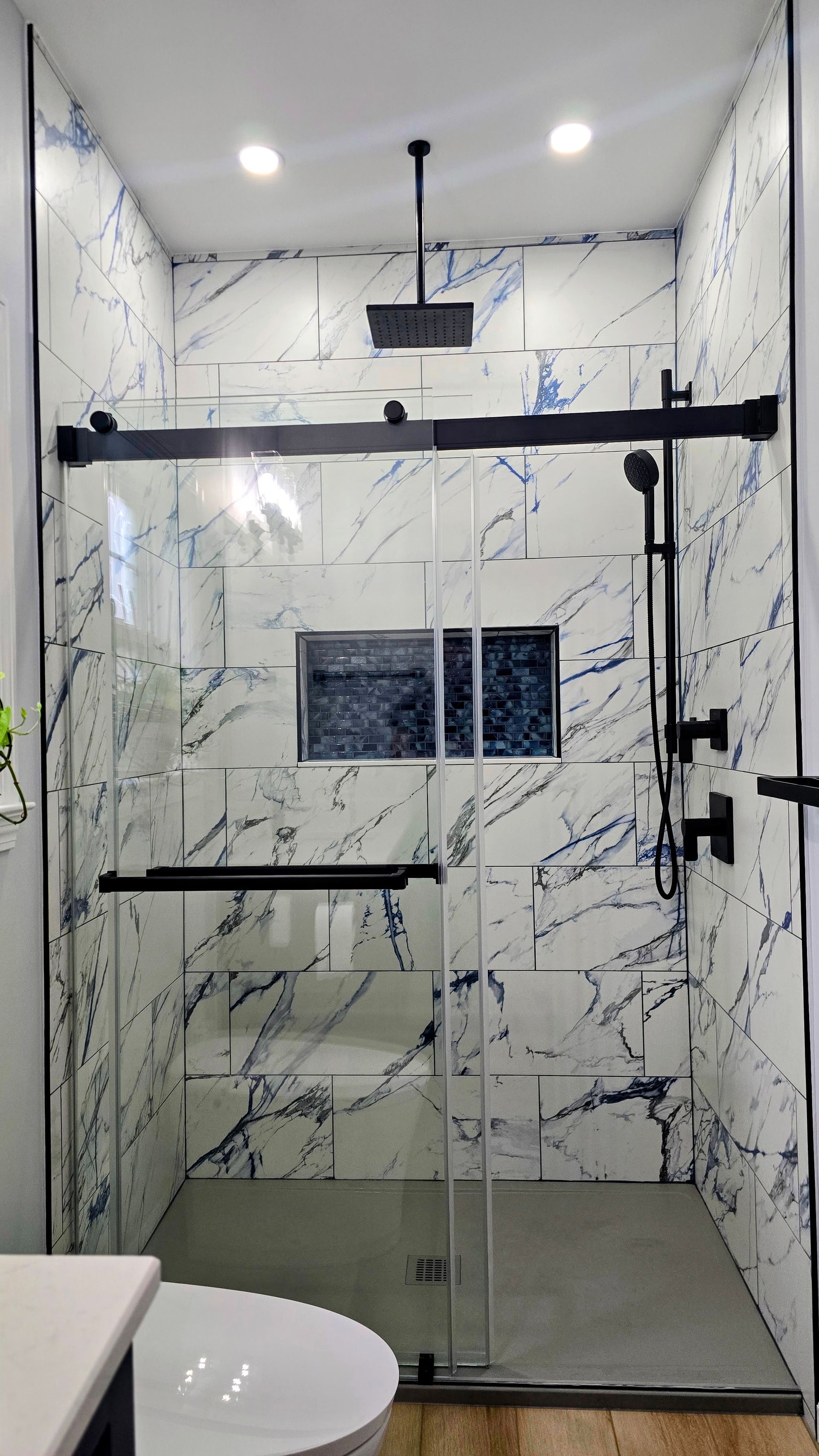 Marble-tiled shower with a clear sliding glass door, black fixtures, and a rain showerhead.