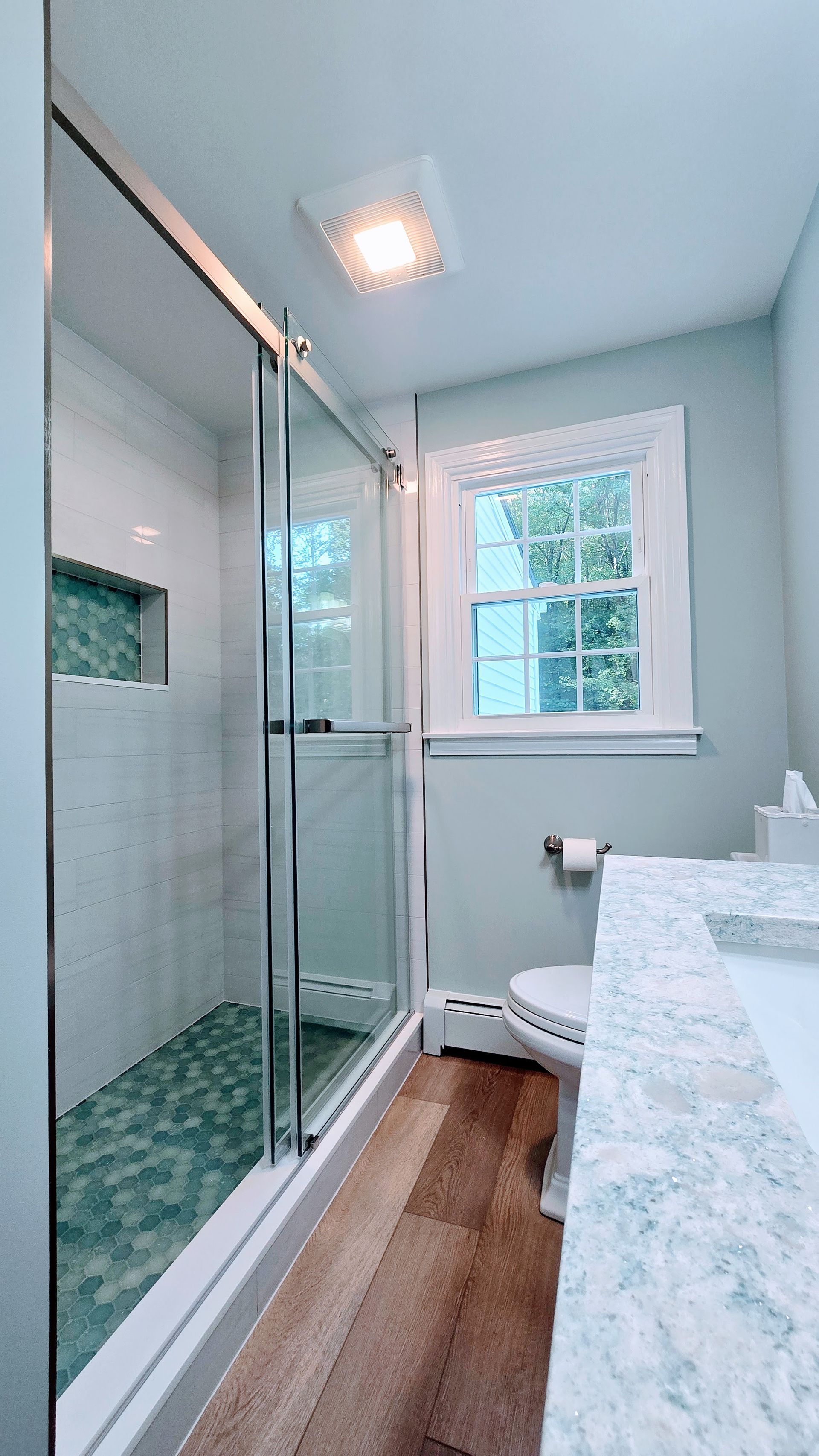 Bathroom renovation in Bristol, CT with a glass shower, toilet, window, and marble countertop.
