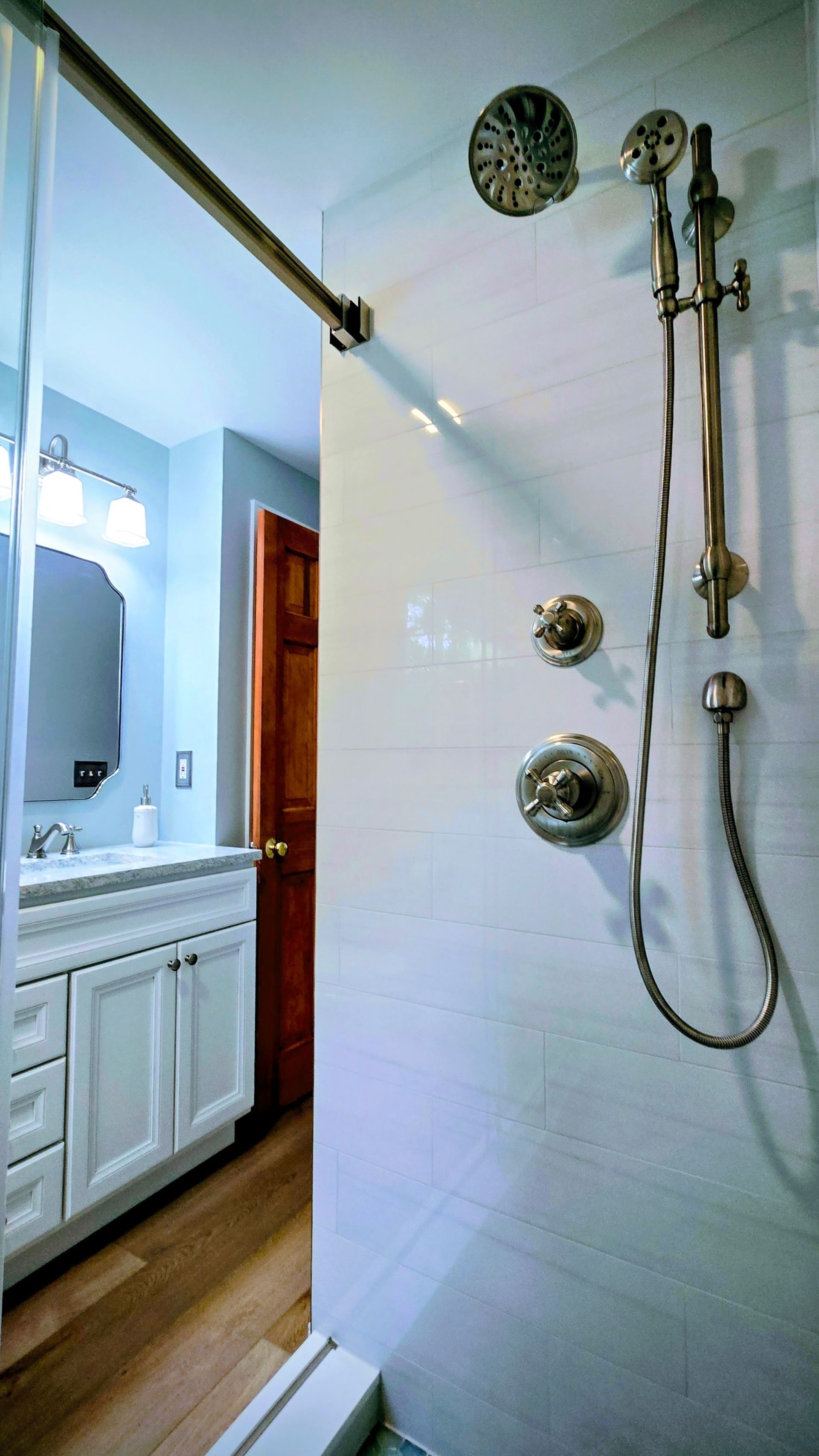 Modern bathroom in Bristol, CT with glass shower, white tile, vanity, and wooden floor.