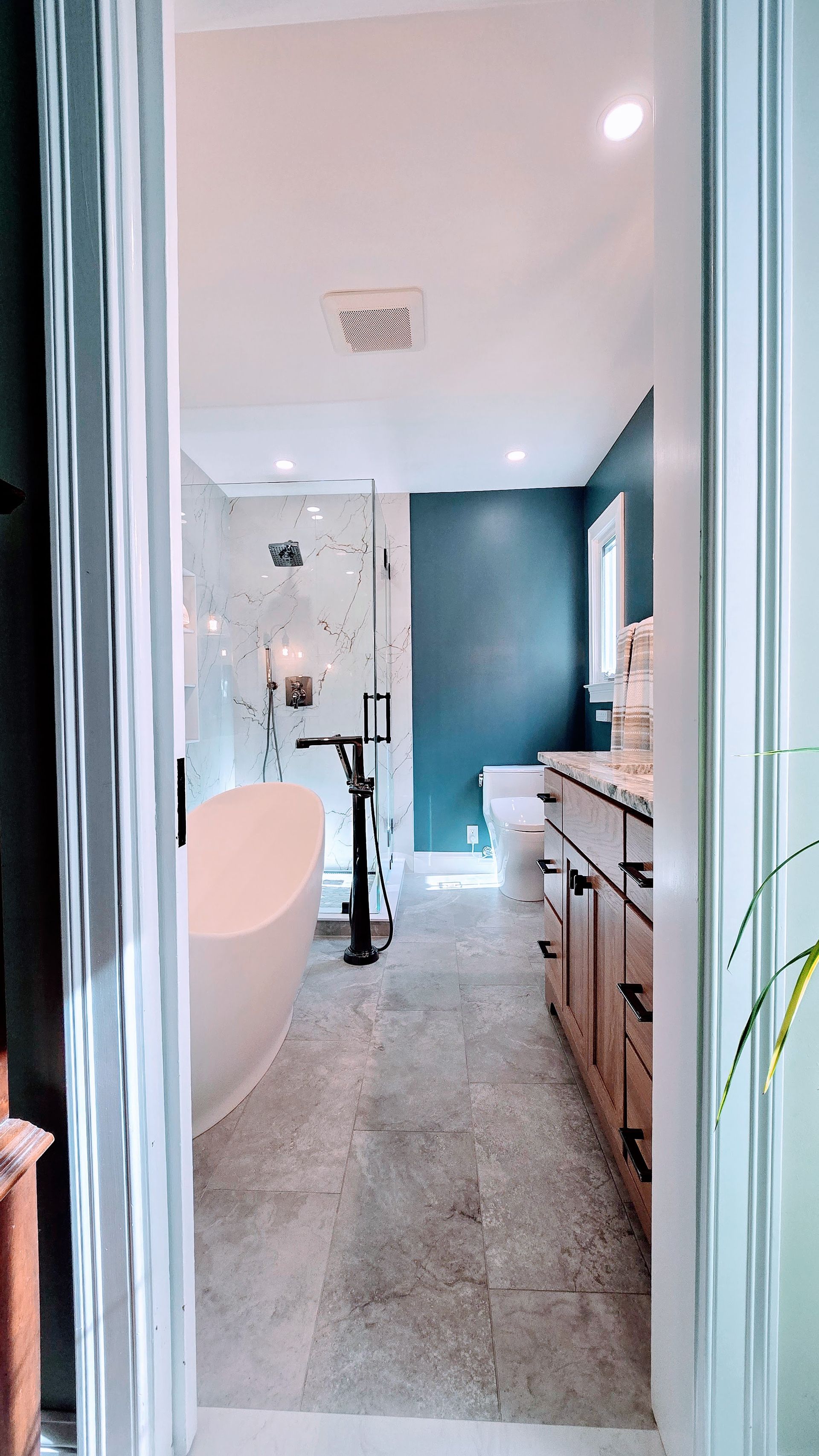 Modern bathroom with a freestanding tub, glass shower, and vanity. Blue walls, wood cabinets.