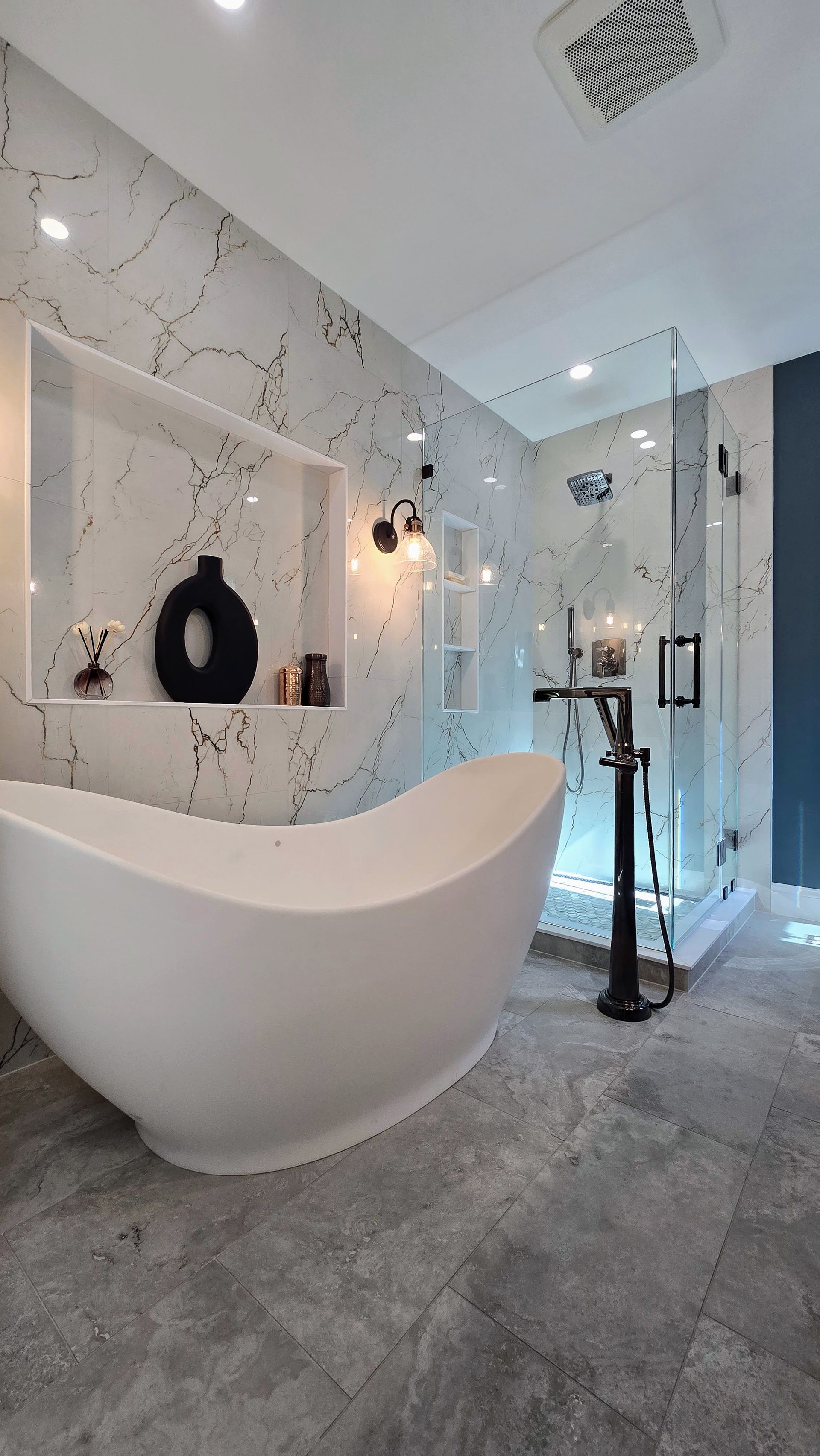 Modern bathroom remodel in Avon, CT with white tub, marble wall, glass shower, and black fixtures.
