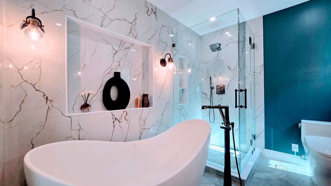 Luxurious bathroom remodel in Avon CT with white tub, marble walls, glass shower, and teal accent wall.