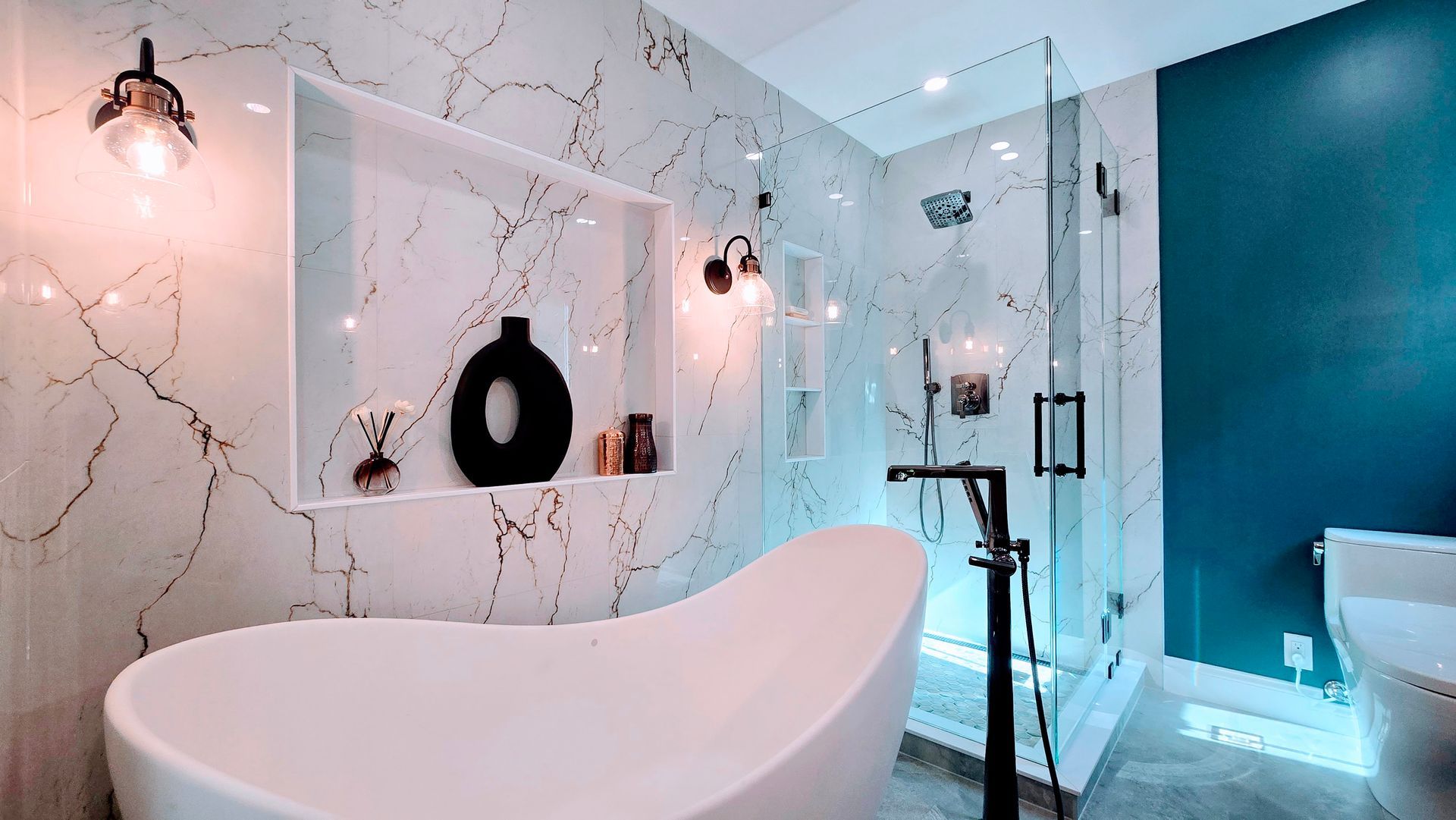 Luxurious bathroom remodel in Avon CT with white tub, marble walls, glass shower, and teal accent wall.