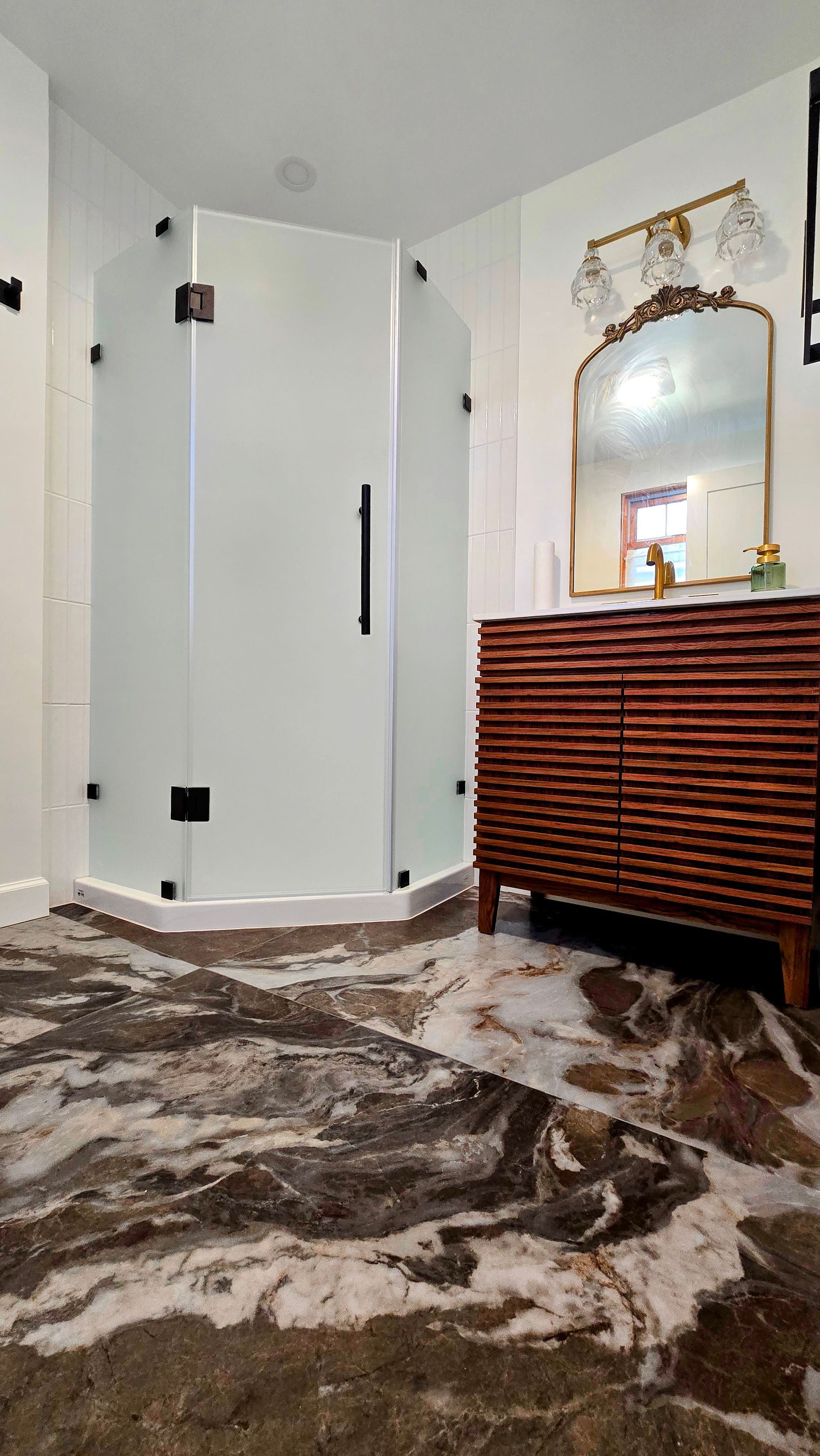 Bathroom with a marble floor, glass shower, and wooden vanity.