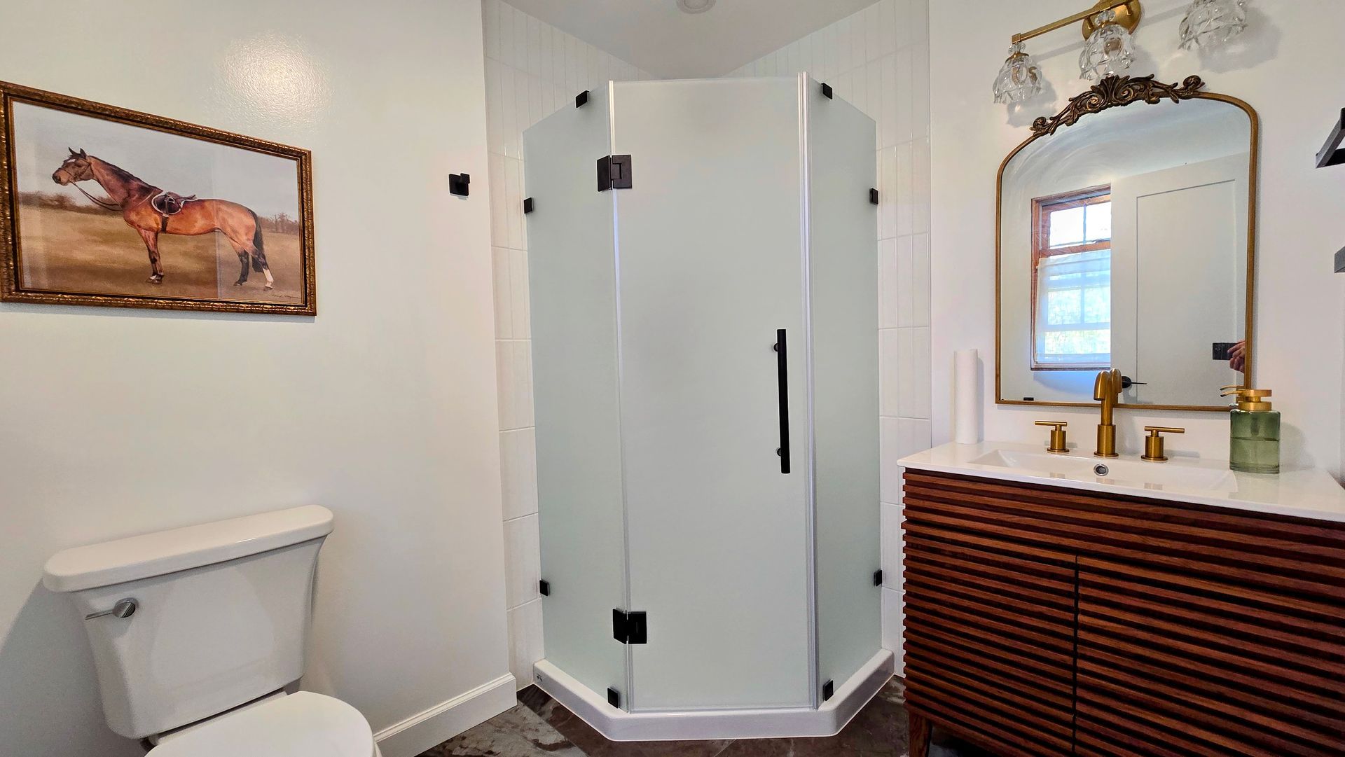 After Bathroom remodel in Simsbury, CT with shower, vanity, toilet, and horse painting. White walls, gold fixtures, and dark wood vanity.
