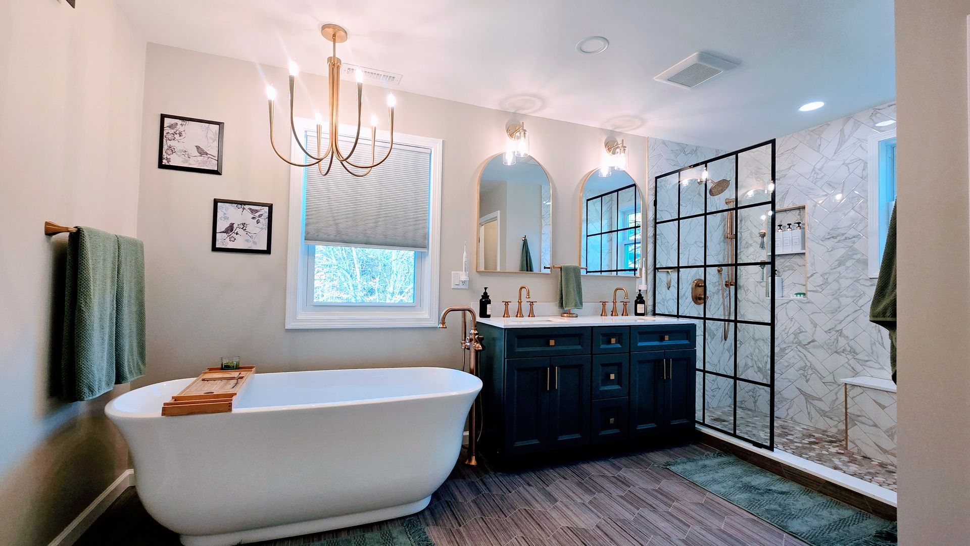 Elegant bathroom renovation in Wolcott, CT with a dark blue vanity, a white soaking tub, and a glass-enclosed shower.