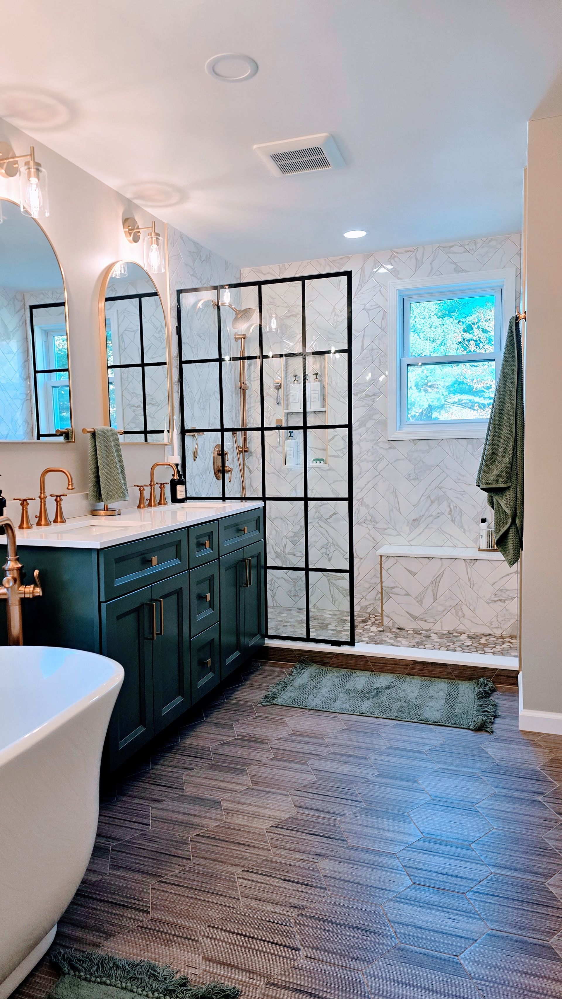 Elegant bathroom in Wolcott, CT with a dark green vanity, marble shower, and a white soaking tub.
