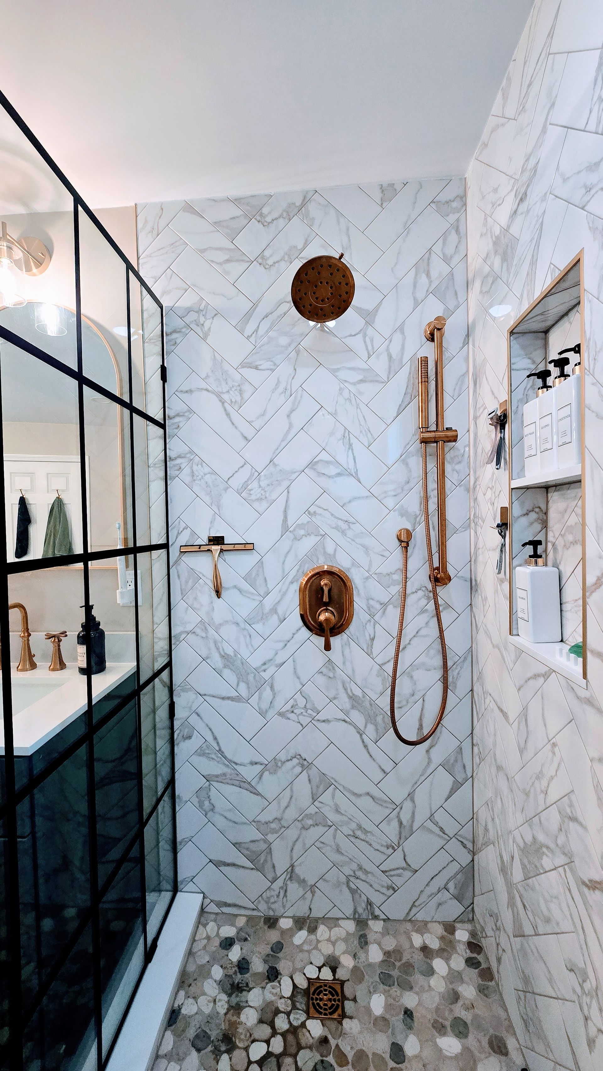 Luxurious walk-in shower renovation in Wolcott, CT with herringbone tile, bronze fixtures, glass enclosure, and a built-in shelf.