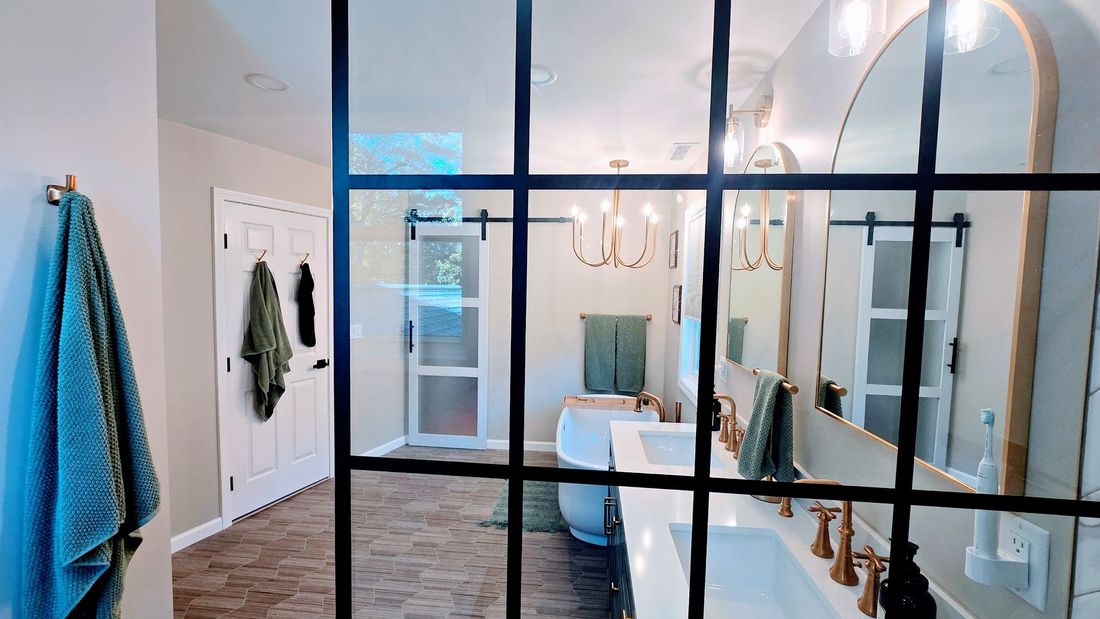 Bathroom remodeling in Wolcott, CT with glass-paneled partition, white vanity, and gold fixtures. Green towels and a hanging chandelier are visible.